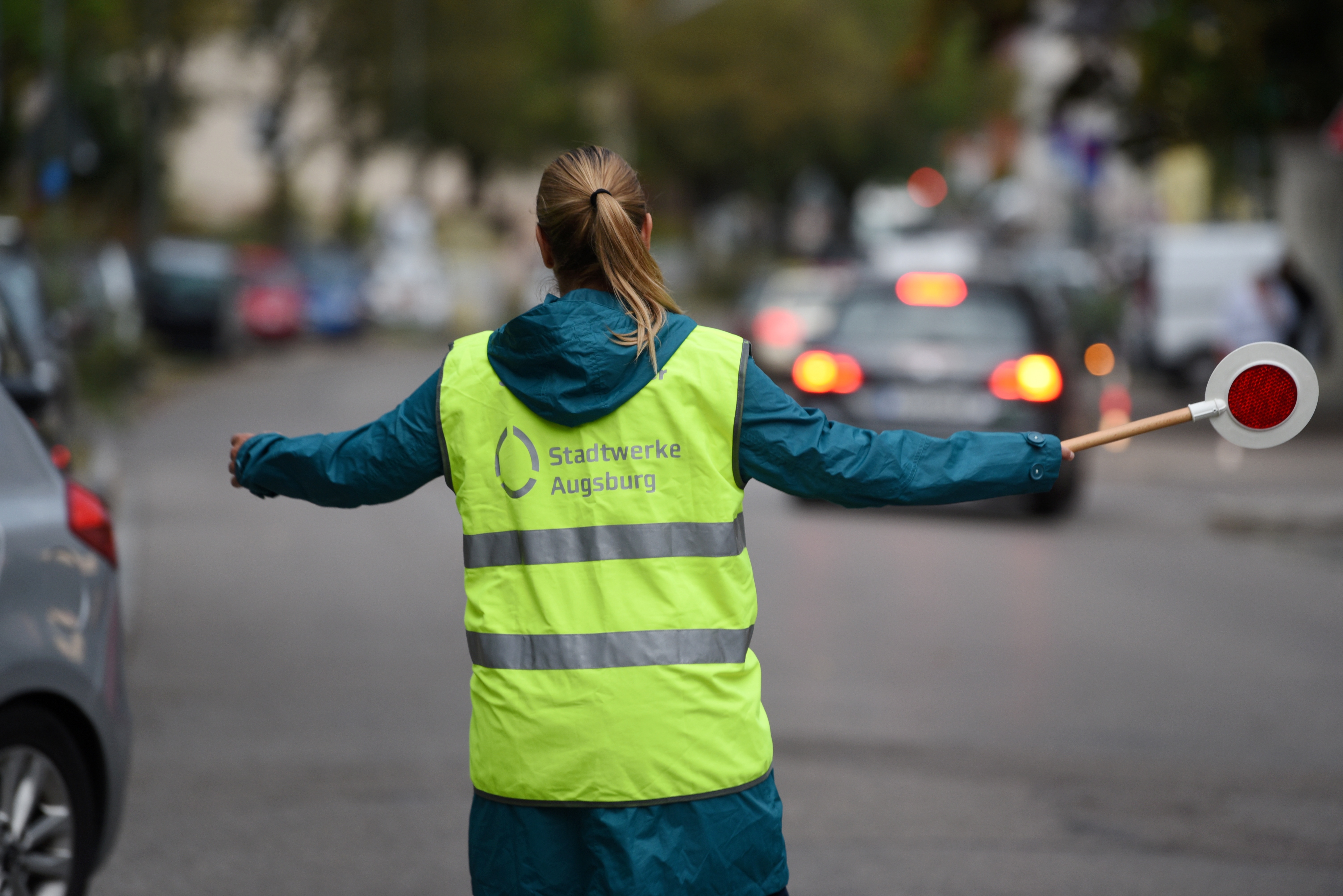 Eine Frau steht mit einer gelben Warnweste und mit einer Polizei-Kelle auf der Straße 