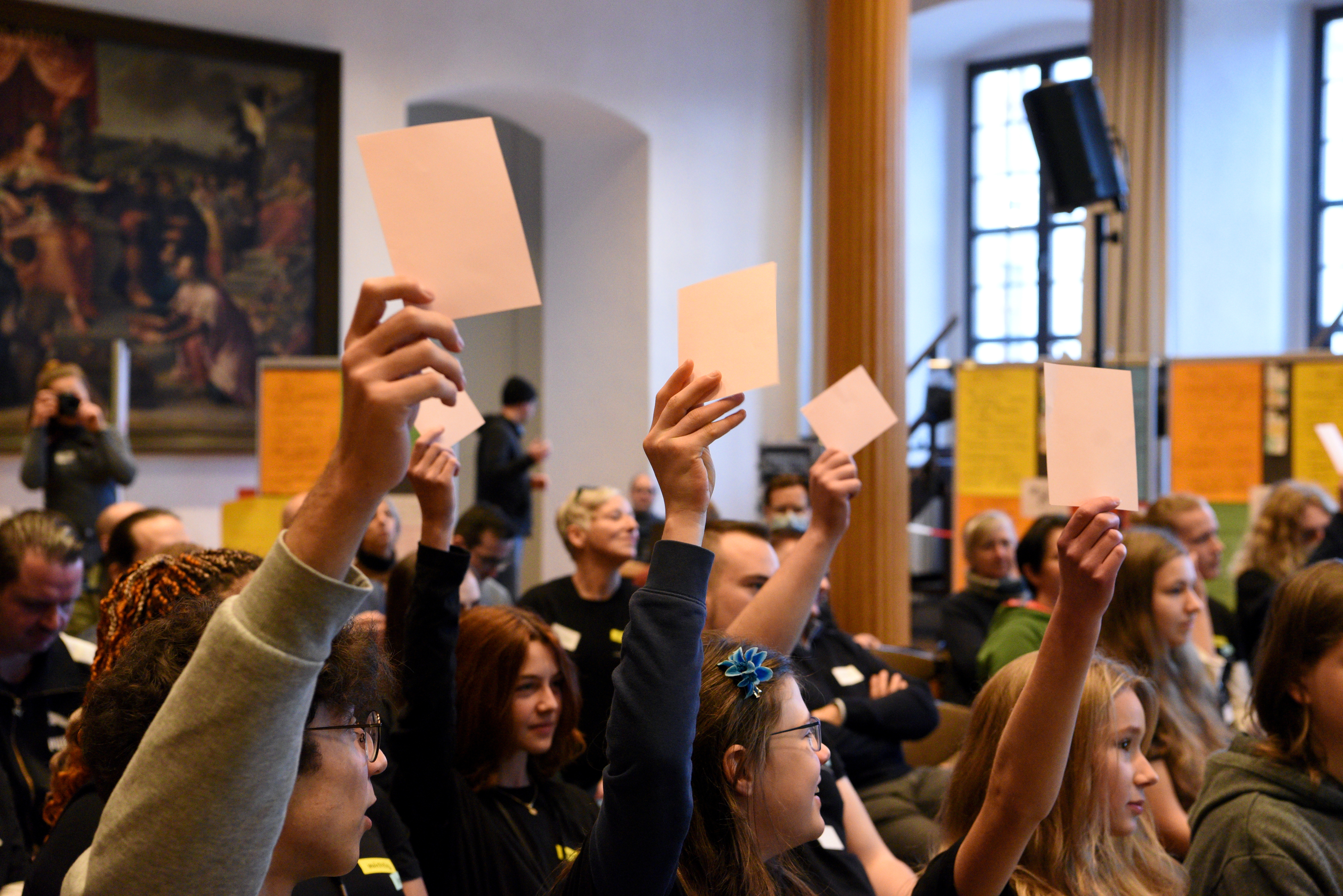 In einem Saal des Rathauses sitzen viele junge Menschen. Einige heben Zettel zu einer Abstimmung in die Luft.