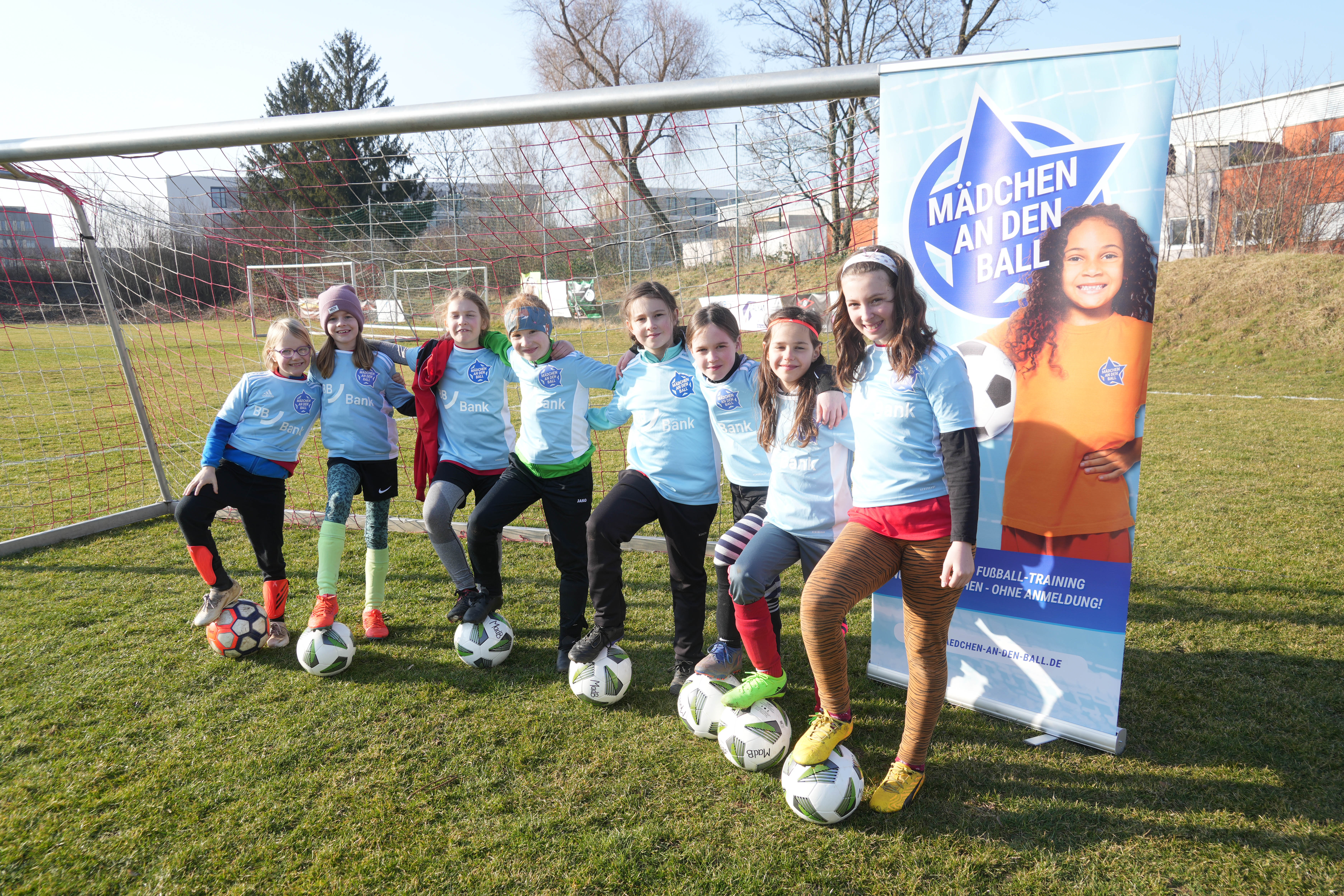 Acht Mädchen in Fußballkleidung stehen vor einem Fußballtor