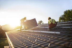 Zwei Mänbner im Blaumann montieren auf einem Dach Solarpanels.