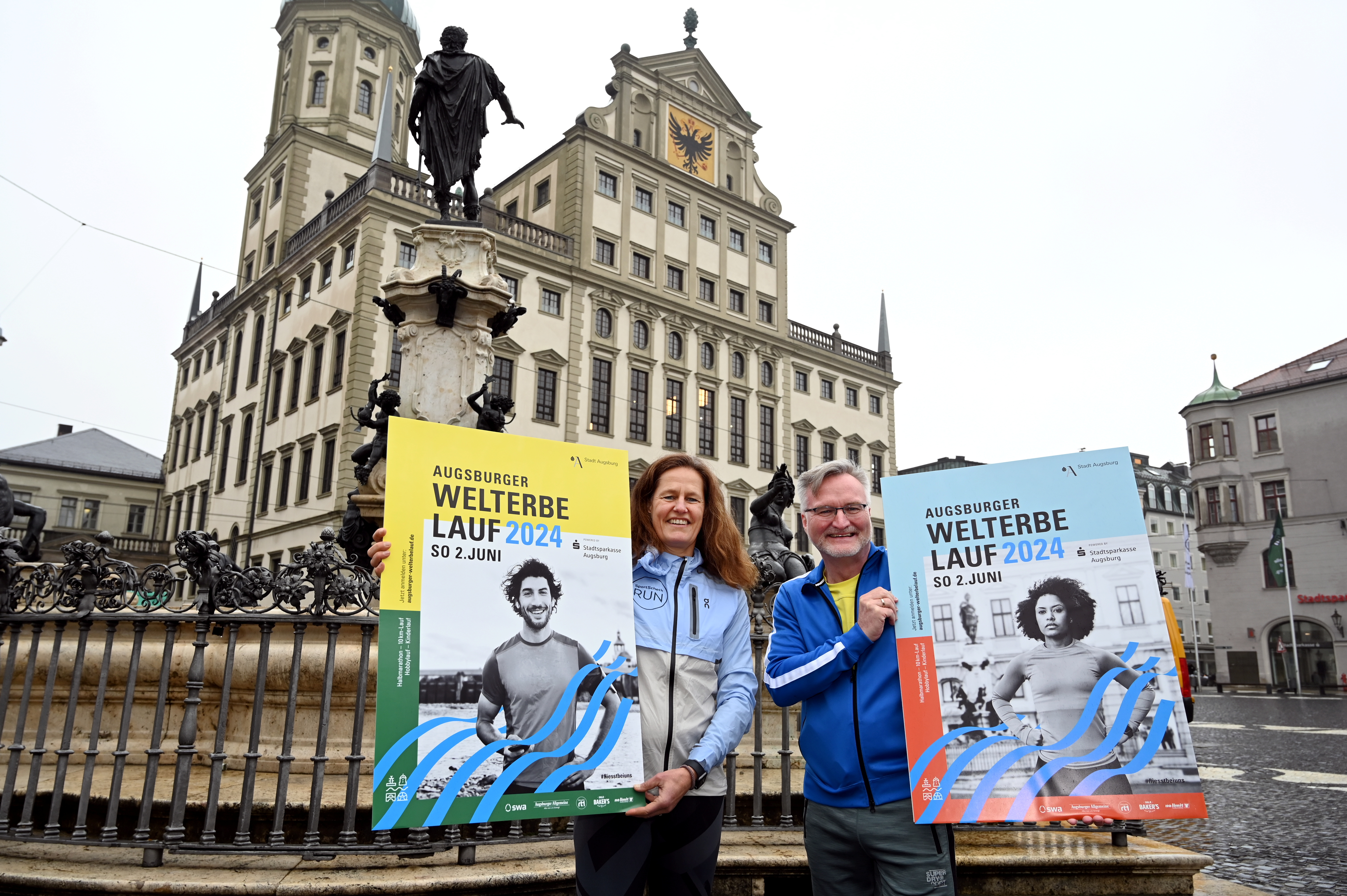 Agenutrinhaberin Katja Mayer und Sportreferent Jürgen Enninger stehen auf dem Rathausplatz und halten die Werbeplakate zum Welterbelauf hoch.