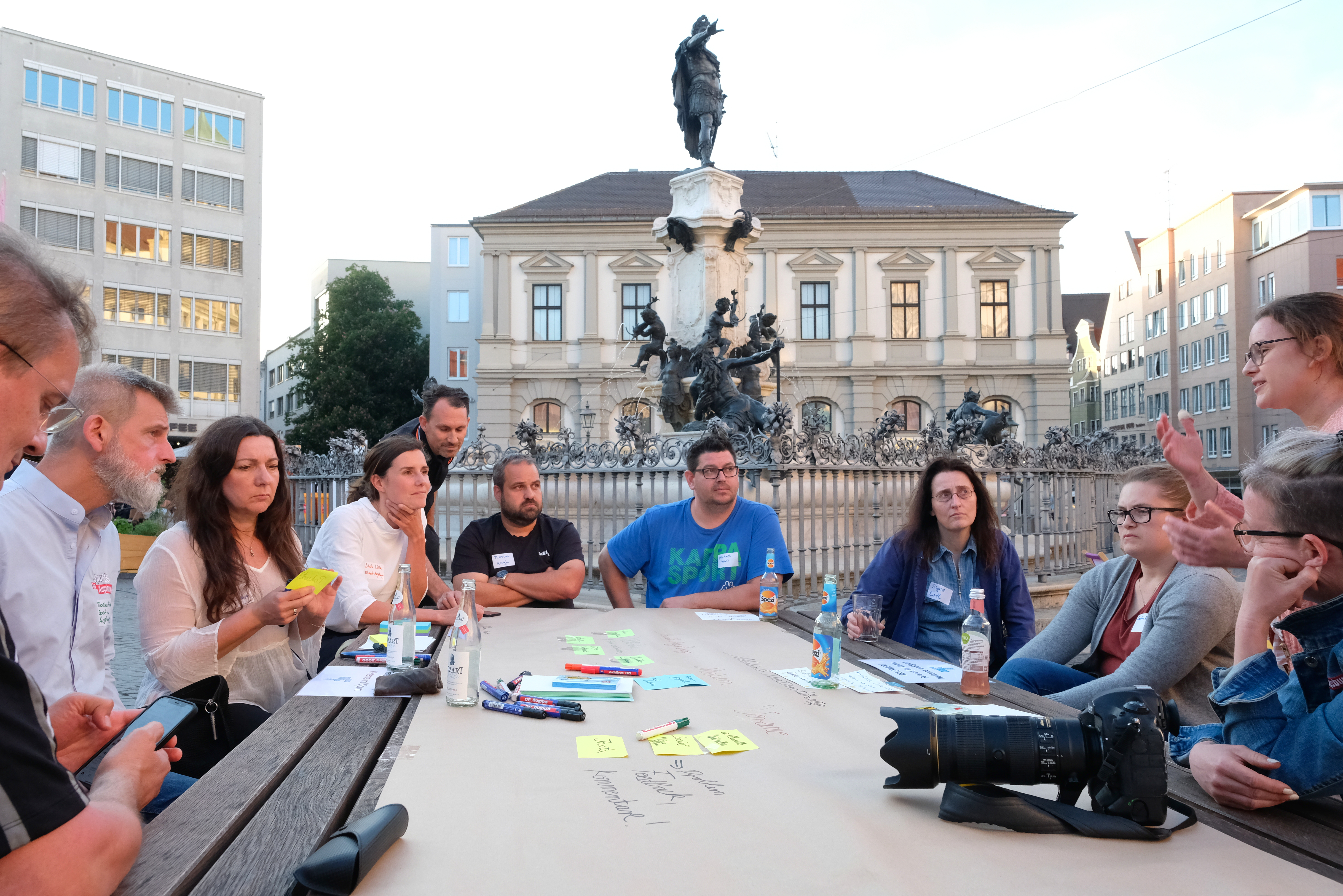 Eine Gruppe von Menschen sitzt vor dem Augustusbrunnen an einem Tisch.