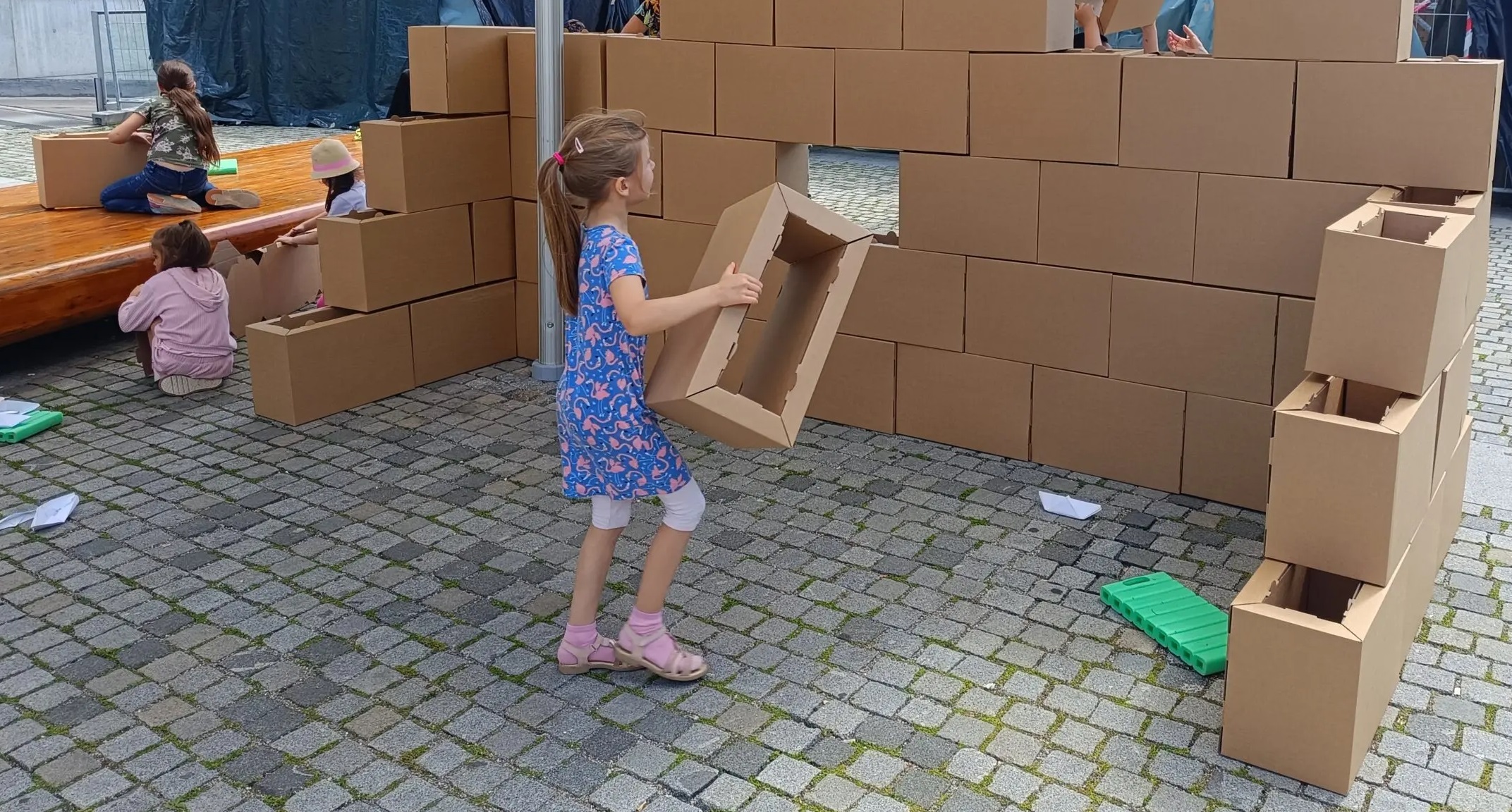 Kinder falten Kartons und bauen daraus eine Mauer
