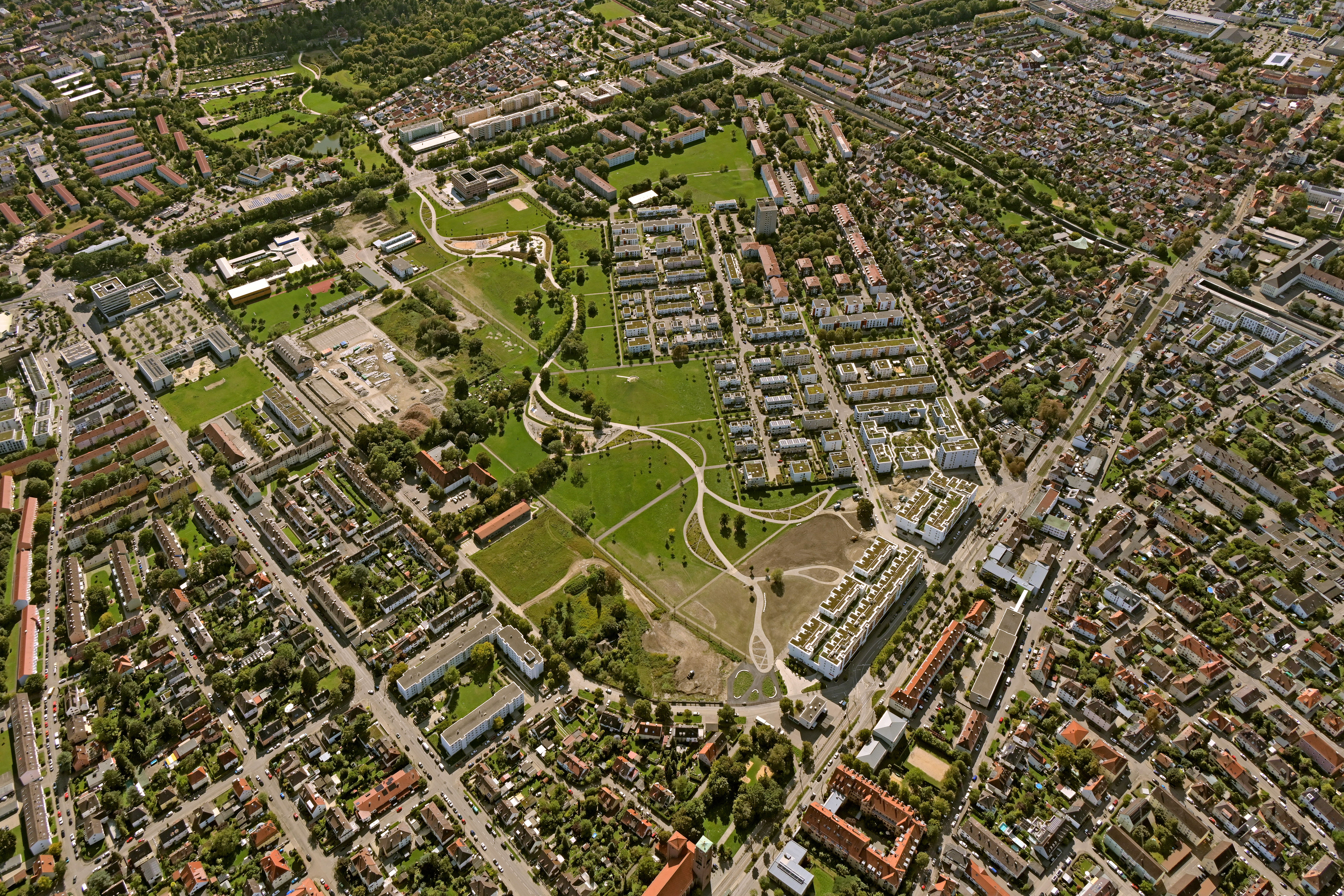Das Foto zeigt eine Luftaufnahme von einem Teil des Westparks. Dabei sieht man viele Grünflächen und einen hellen Weg, der geschwungen über die Wiesen verläuft.