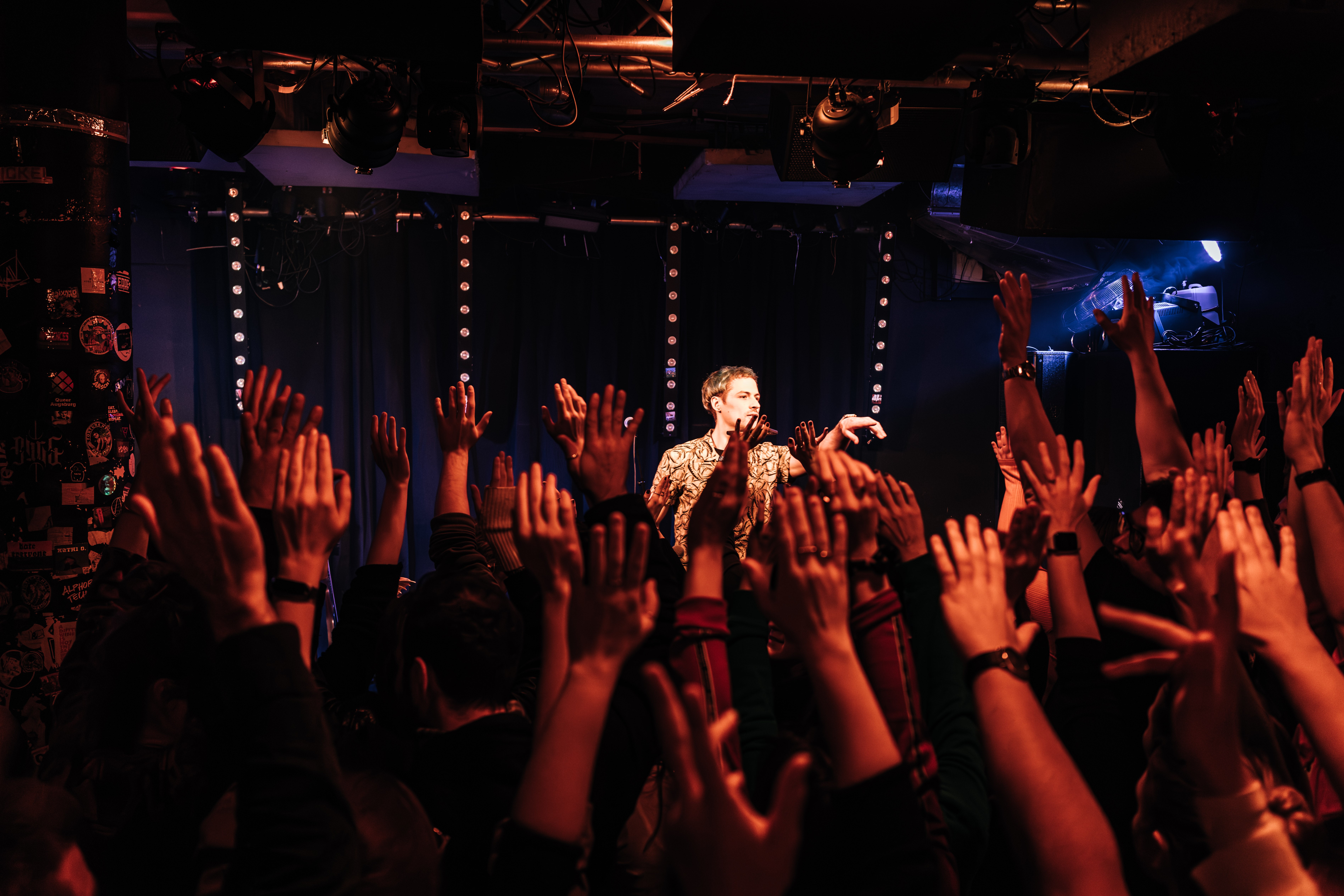 Bei einem Konzert strecken die Besucher die Hände in die Höhe. Auf der Bühne steht ein Moderator