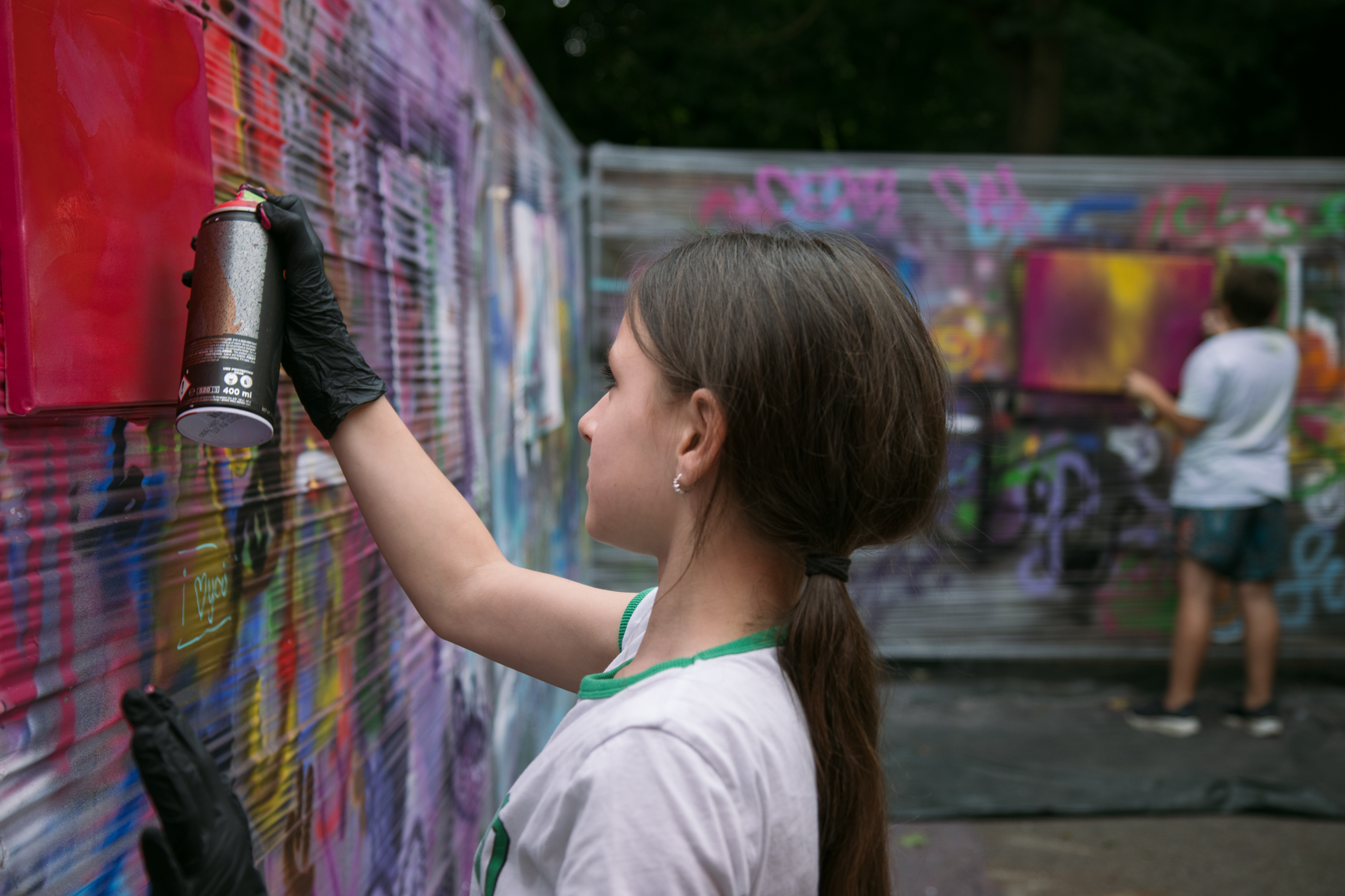 Ein Mädchen sprüht mit einer Spraydose ein buntes Bild an eine Graffiti-Wand