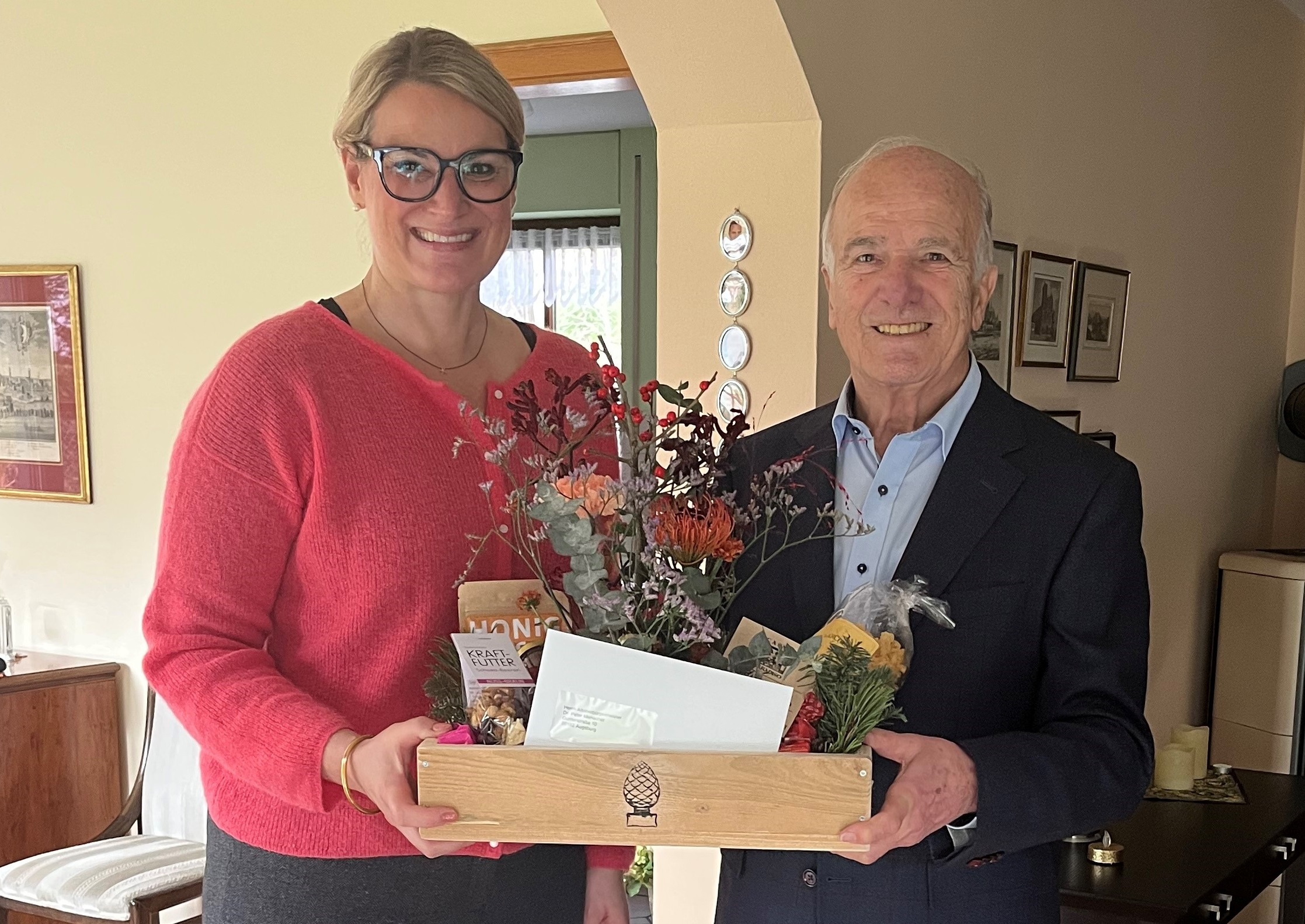 OB Eva Weber überreicht Dr. Peter Menacher eine Holzkiste mit dem Wappen der Stadt Augsburg. In der Kiste sind Geschenke
