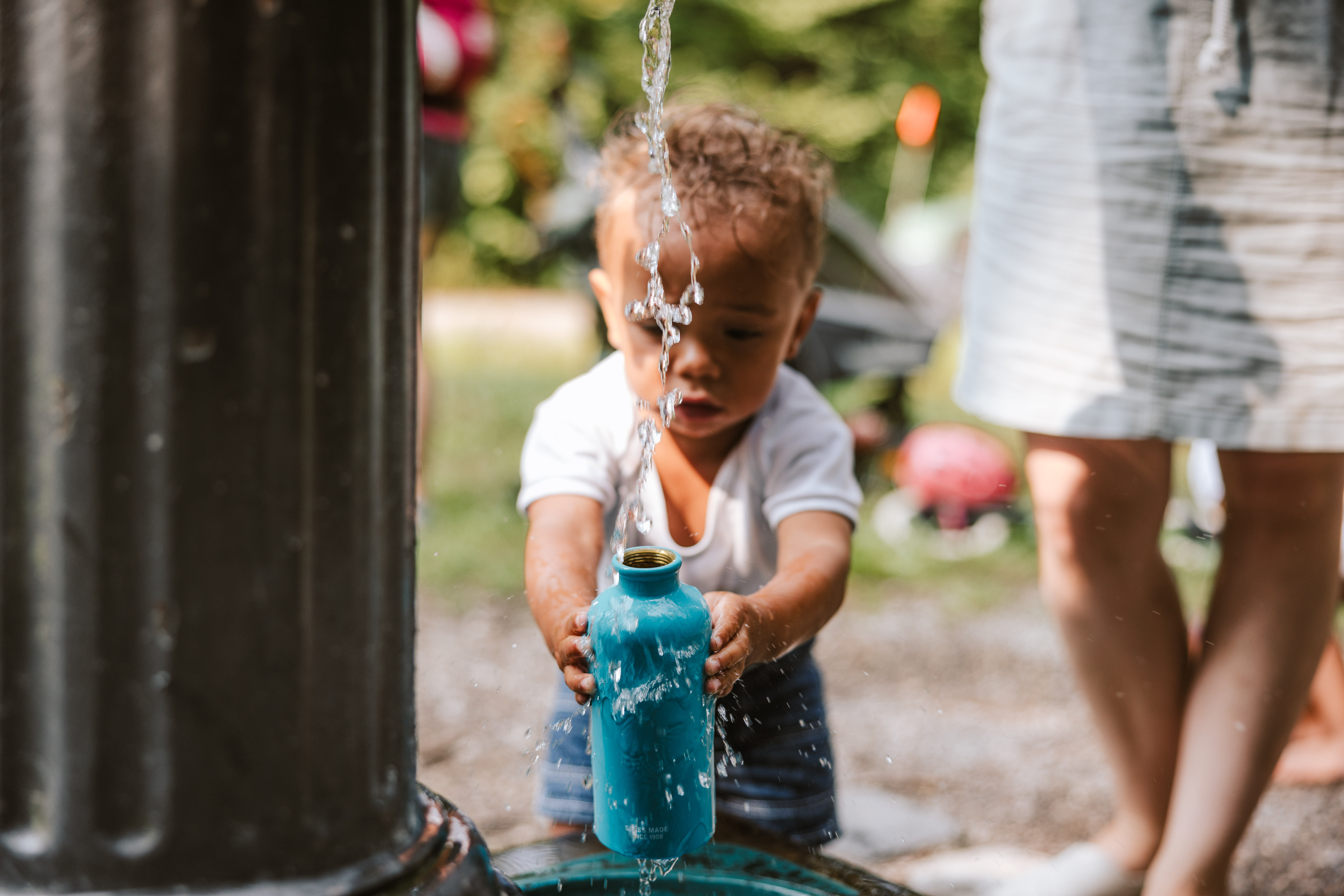 Kleines Kind trinkt am Brunnen Wasser wegen der Hitze