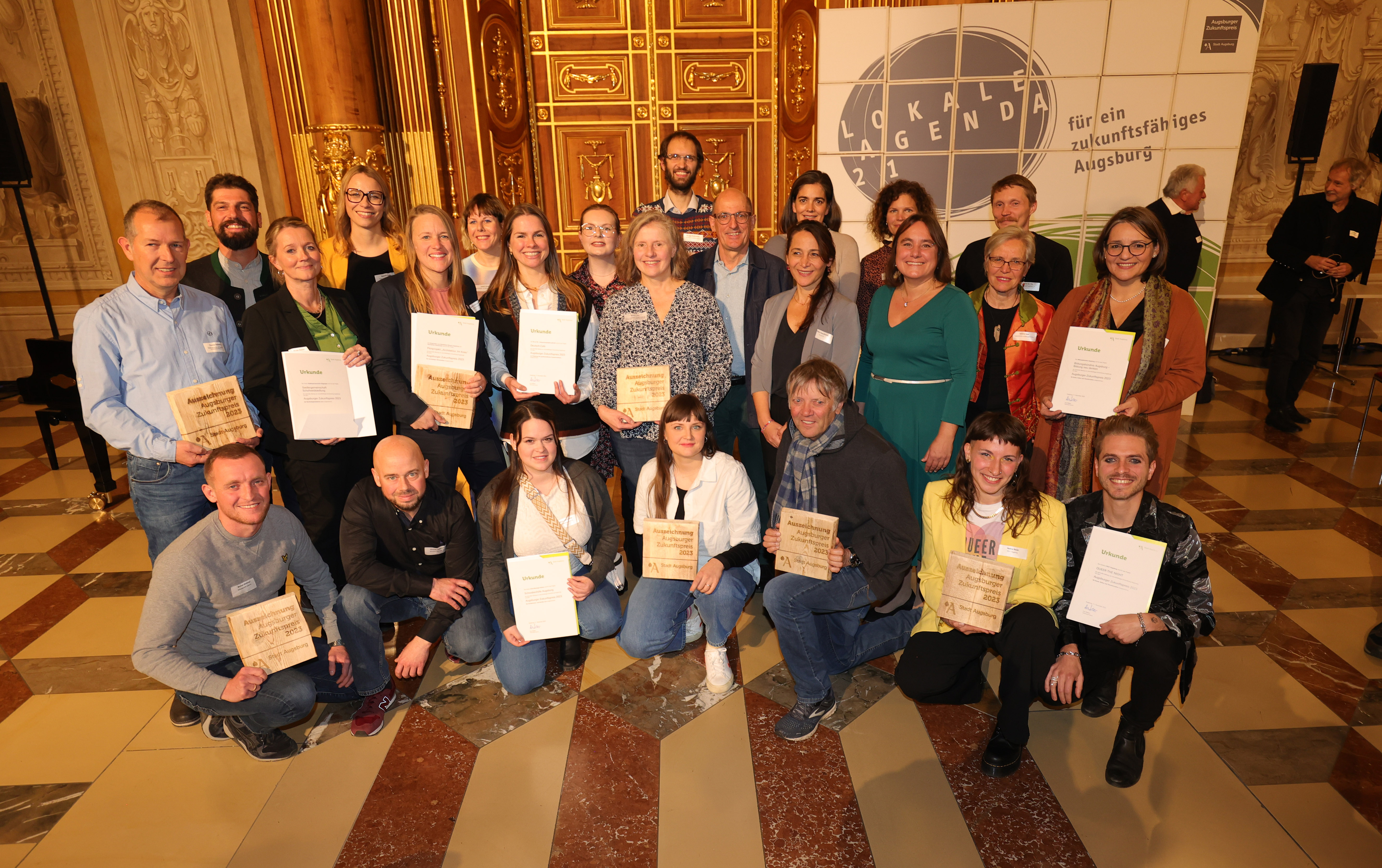 Eine Gruppe von etwa 25 Frauen und Männern im Goldenen Saal des Rathauses. Einige Personen halten Urkunden in den Händen.