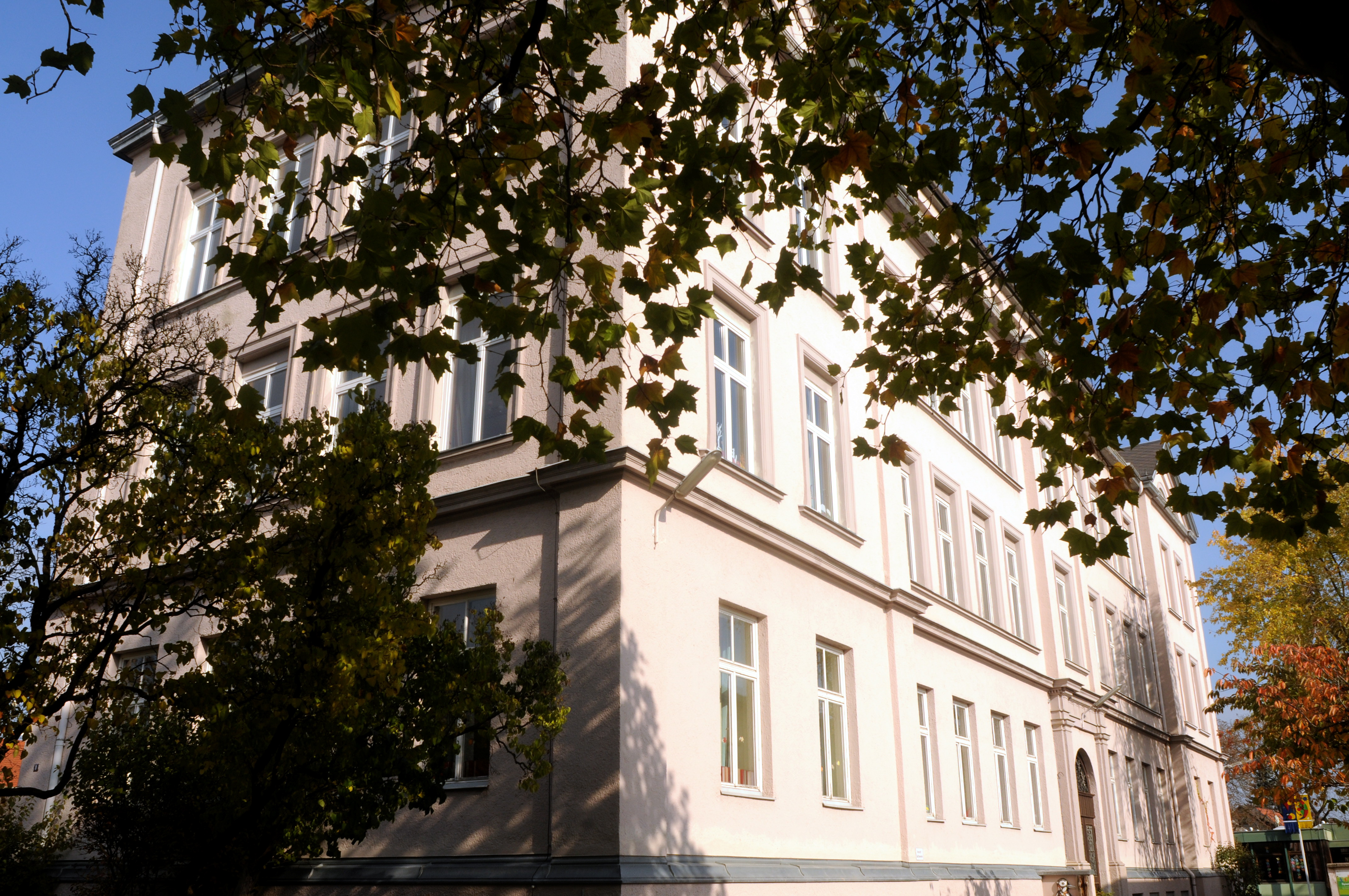 Schulgebäude von außen, unter einem Blätterdach heraus fotografiert