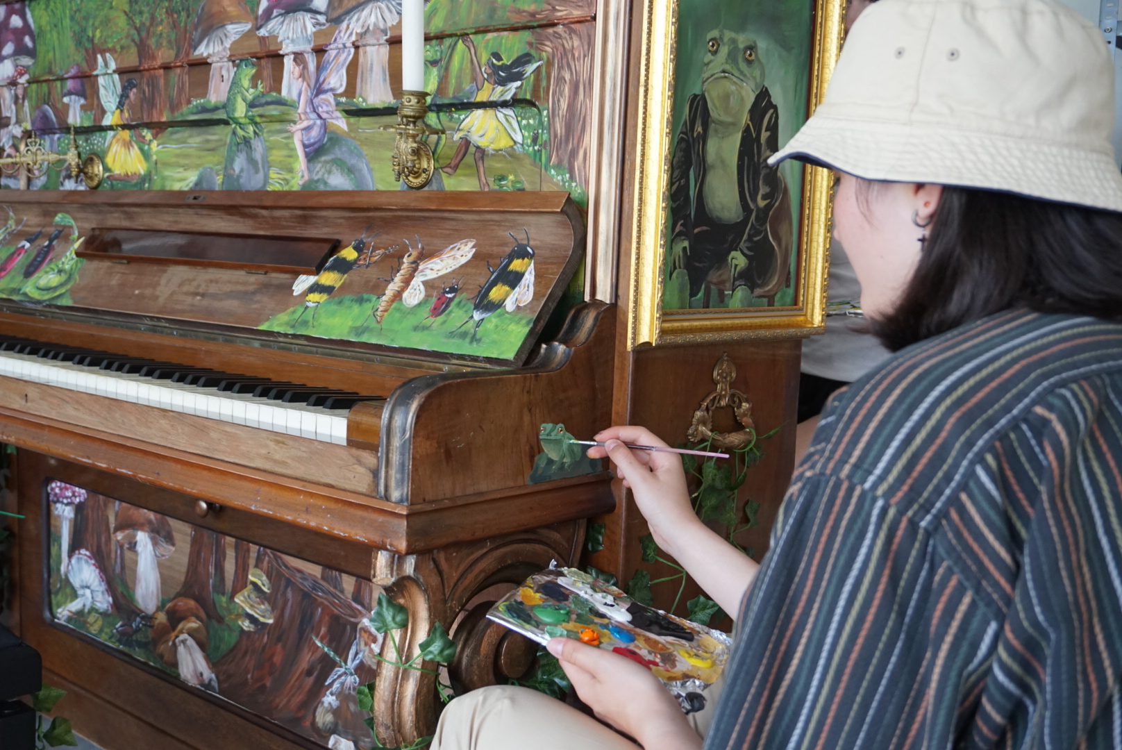Junge Künstlerin bemalt ein Klavier mit Fröschen, Bienen und anderen Tieren.