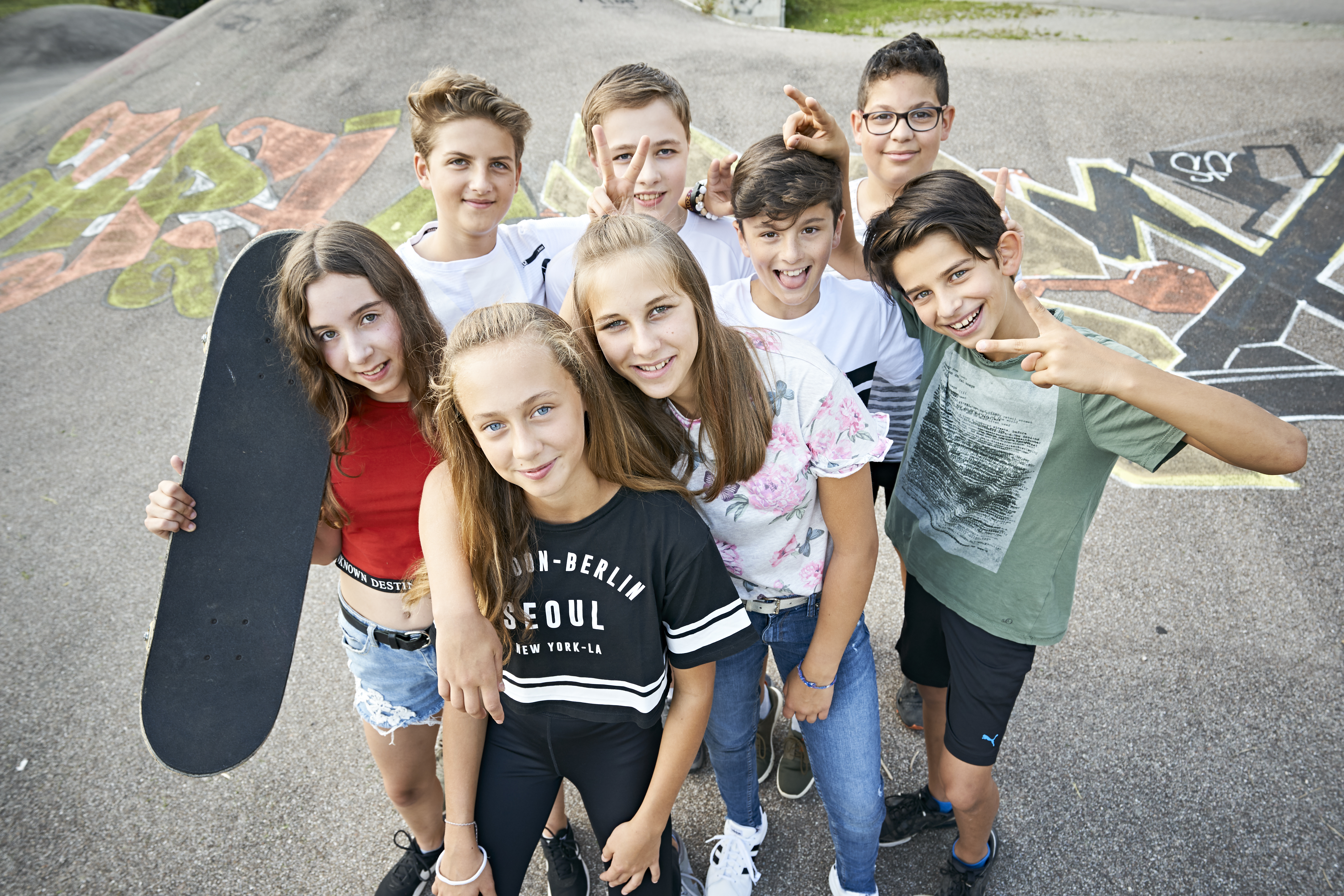 Acht Jugendliche stehen mit Skateboards auf einem Jugendspielplatz