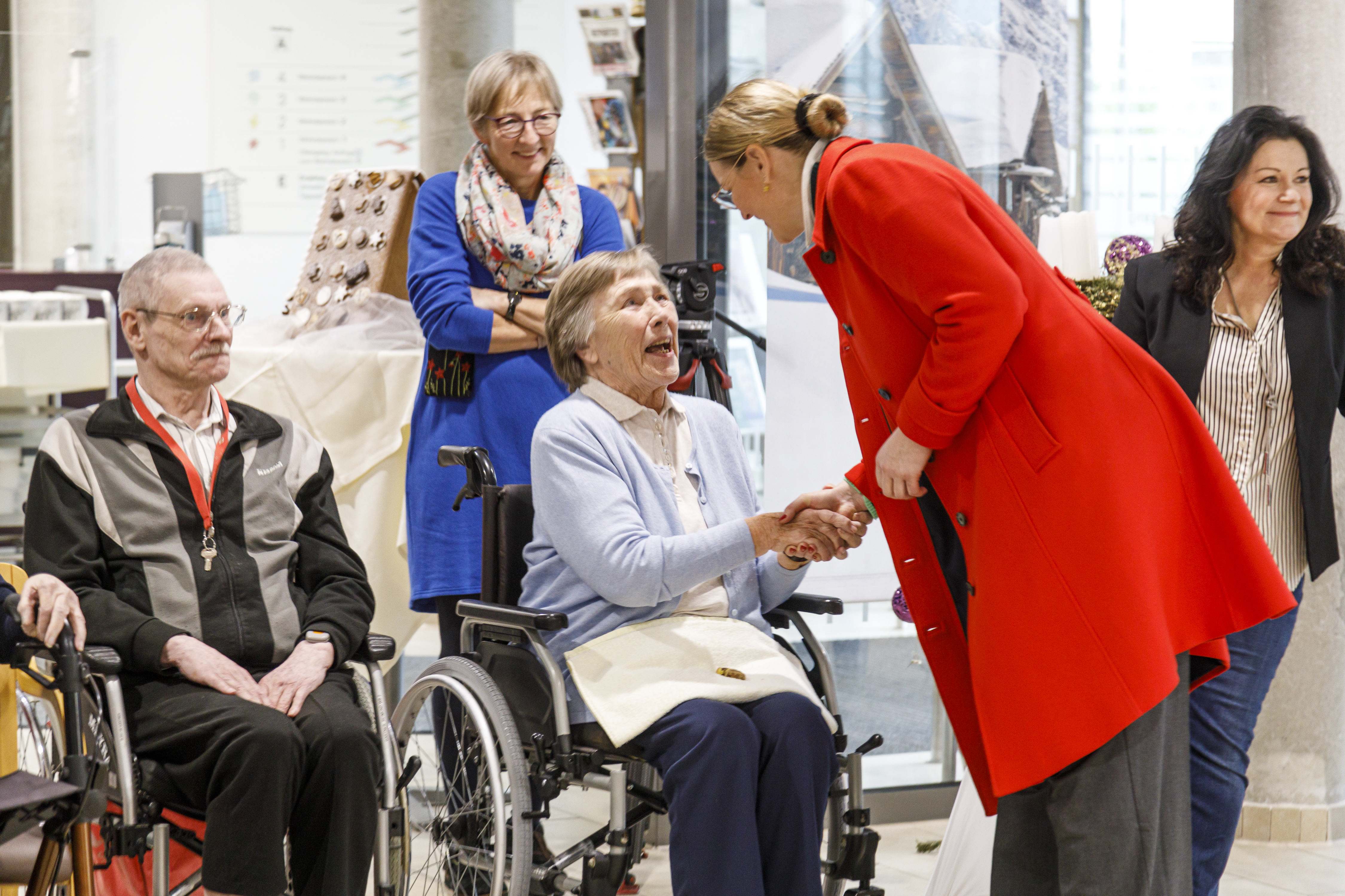 Oberbürgermeisterin Eva Weber reicht einer lächelnden Seniorin im Rollstuhl die Hand.