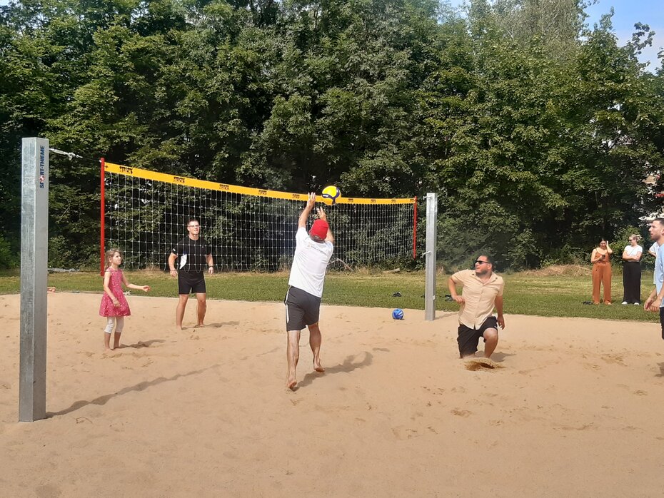Vier Menschen in Sporkleidung spielen Volleyball auf einer Sandfläche