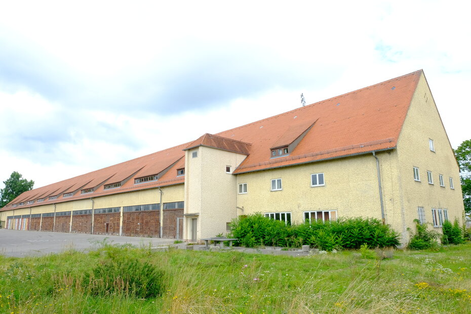 Ein gelbes Gebäude von außen. Man sieht zahlreiche hölzerne Tore, aber nur wenige Fenster.