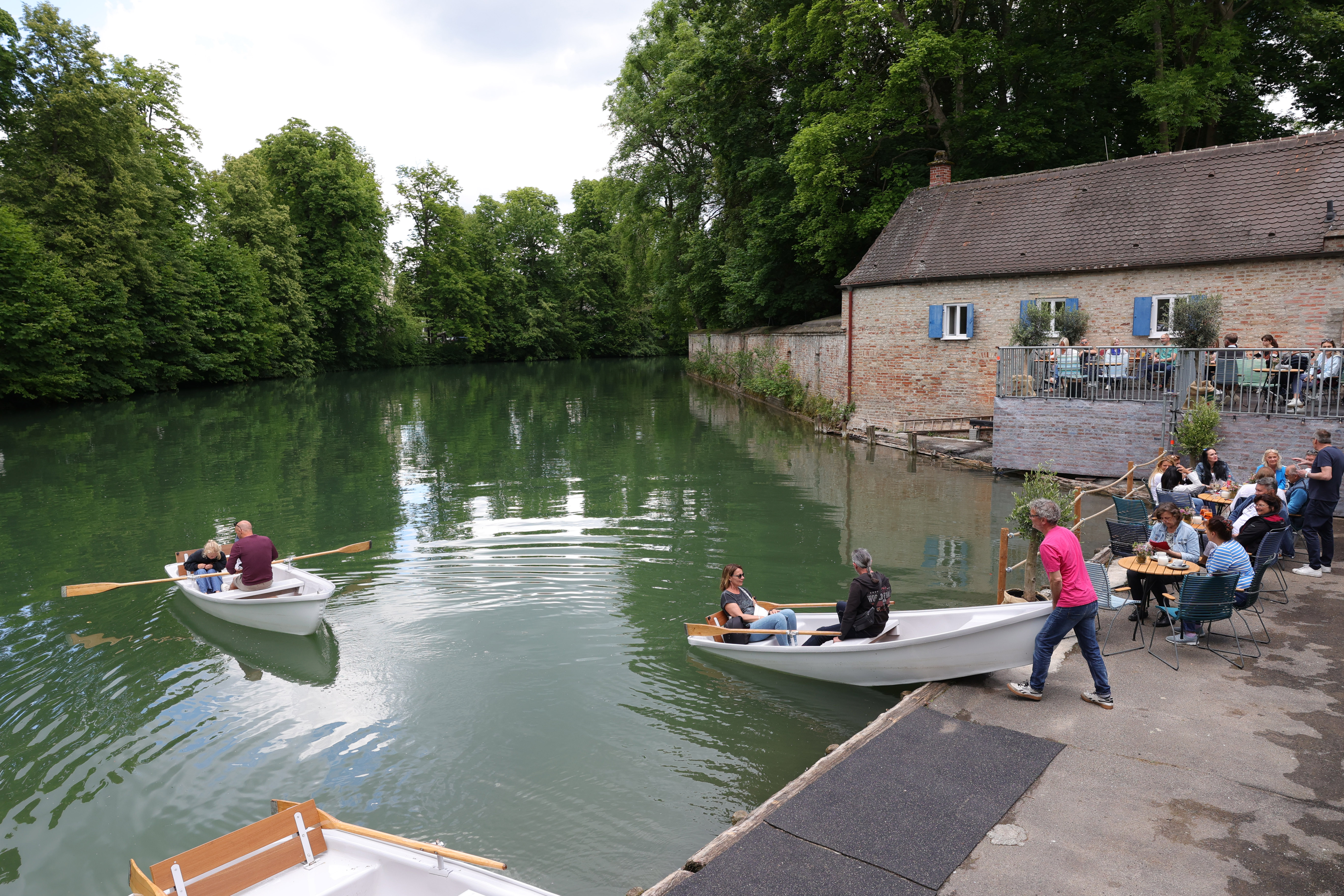 Ein Mann schiebt ein Ruderboot in ein Gewässer. Im Hintergrund ist ein Haus und Teile der historischen Stadtmauer zu sehen