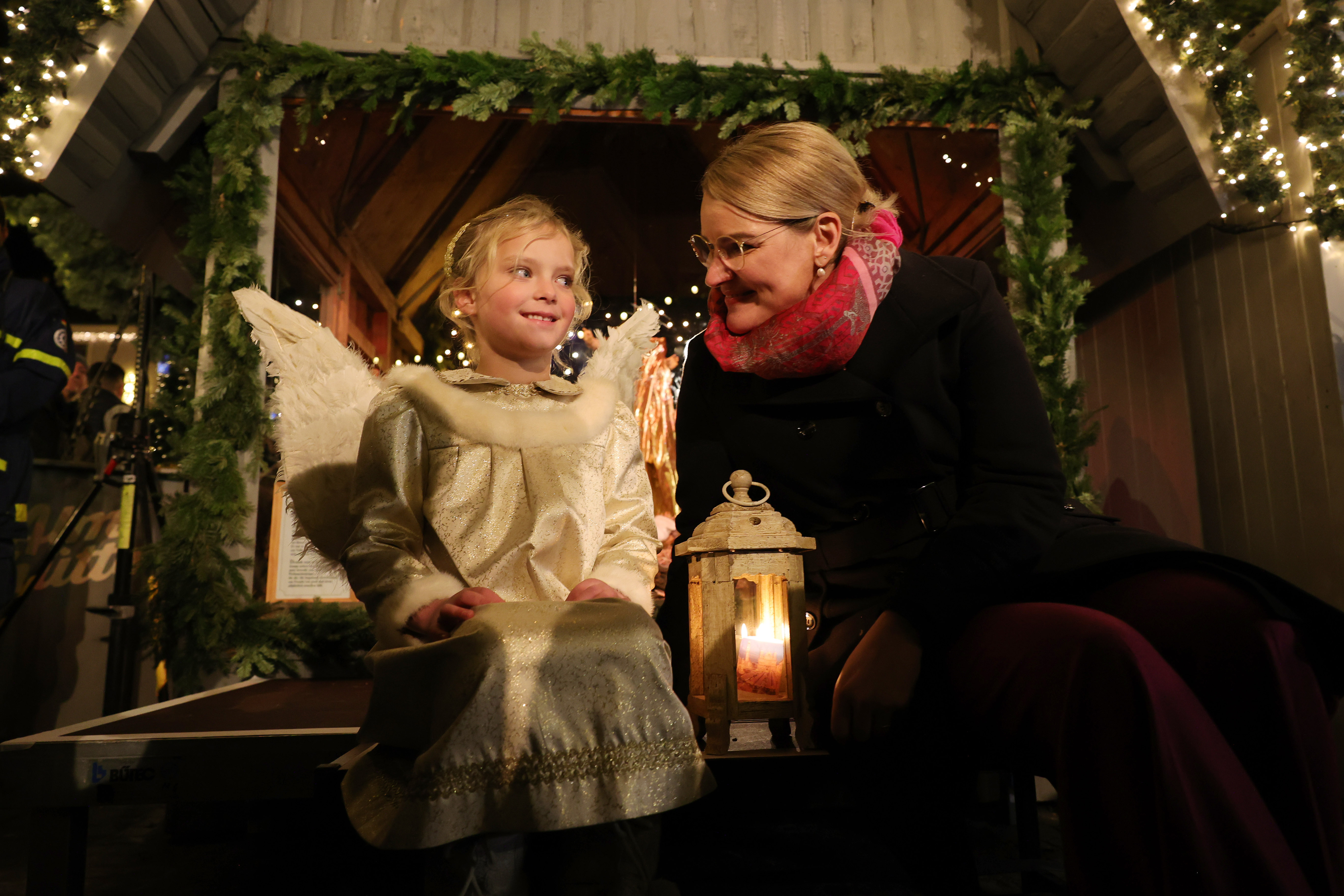Ein Kind im Engel-Kostüm und Oberbürgermeisterin Eva Weber mit einer Laterne vor einem weihnachtlich beleuchteten Stand auf dem Christkindlesmarkt