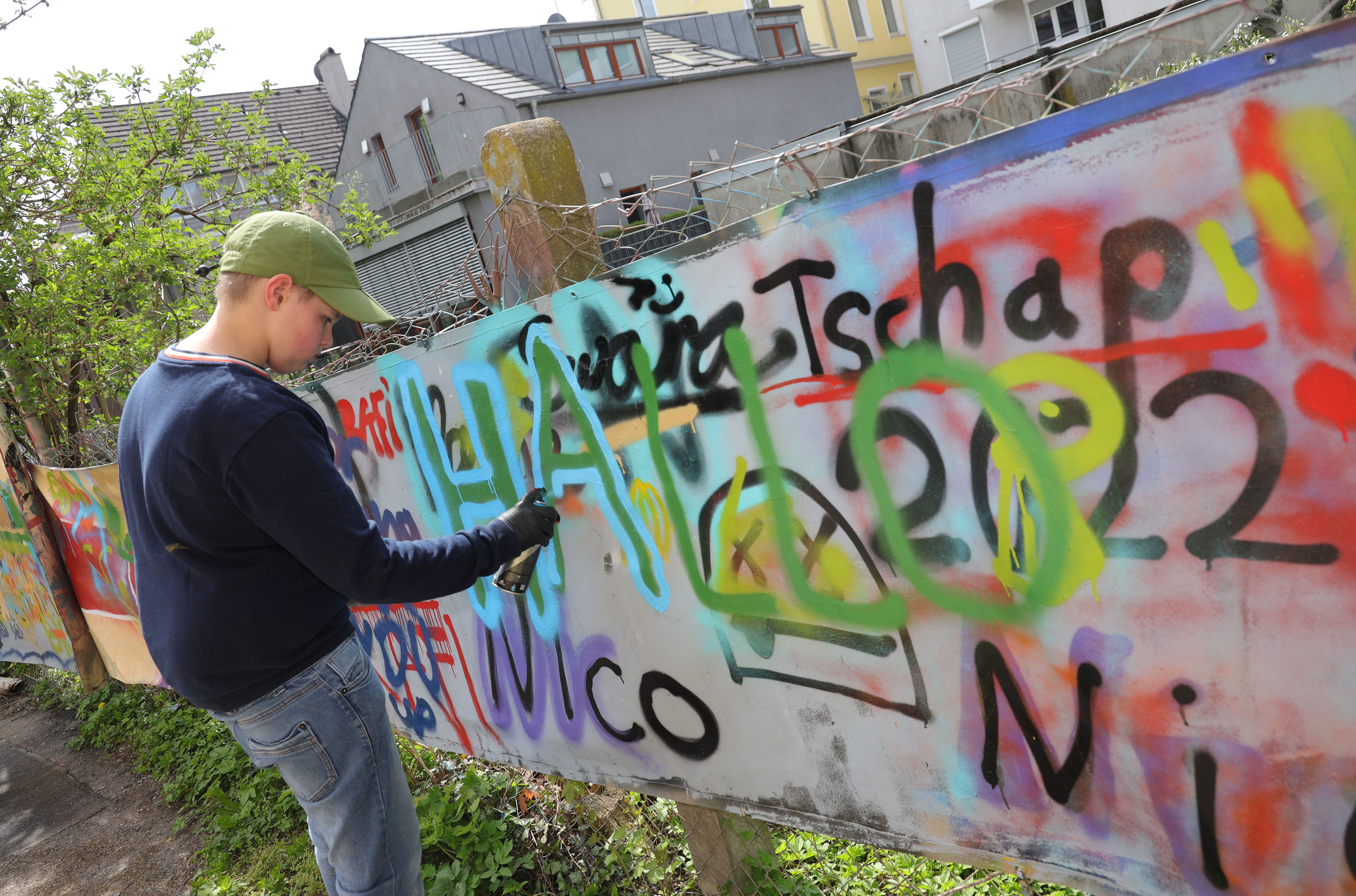 Ein Jugendlicher sprüht ein Graffiti auf eine Wand.