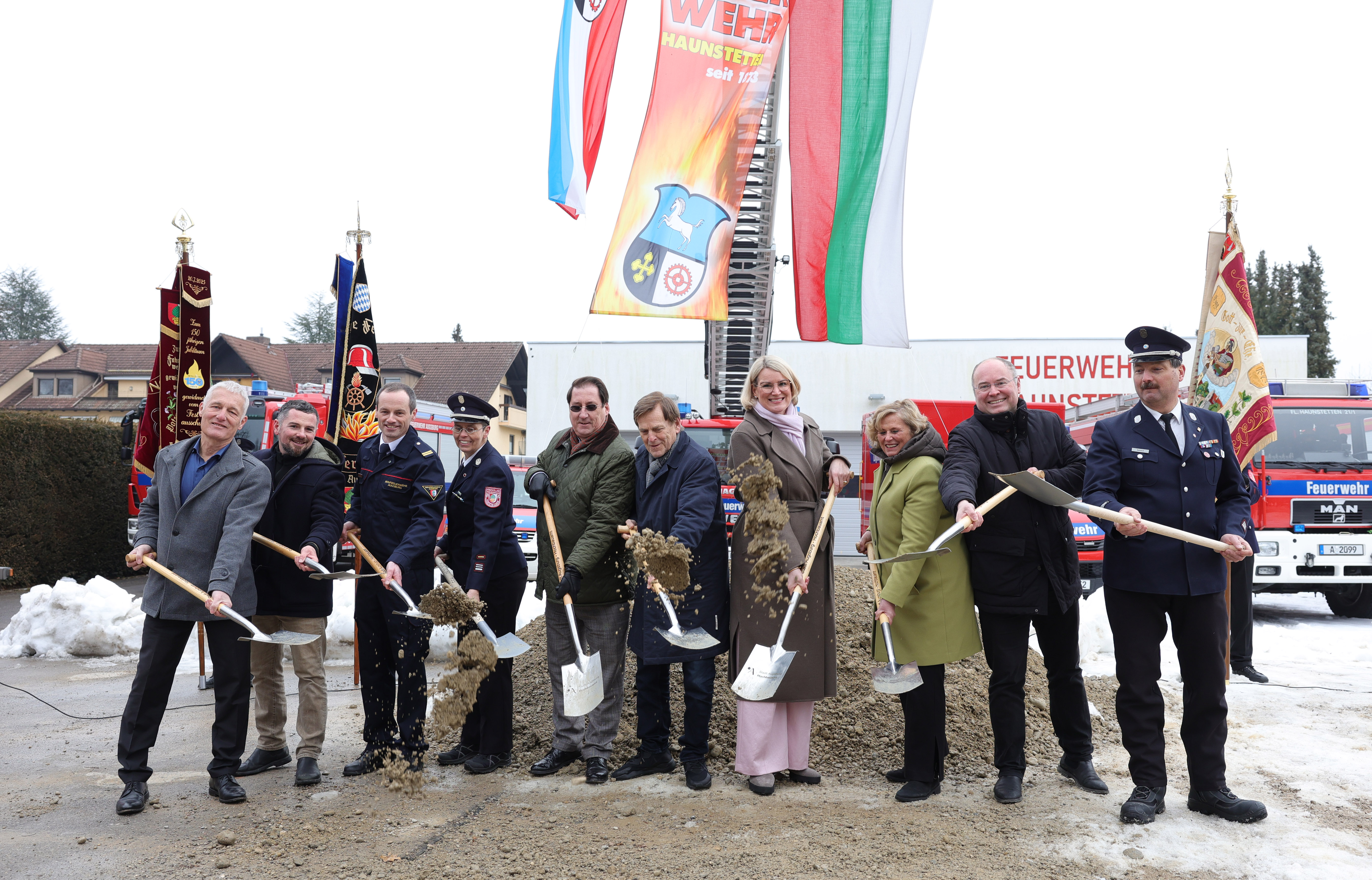 Zehn Leute haben Spaten in den Händen und werfen damit Erde in Richtung Kamera. Einige von ihnen tragen eine Feuerwehr-Uniform.