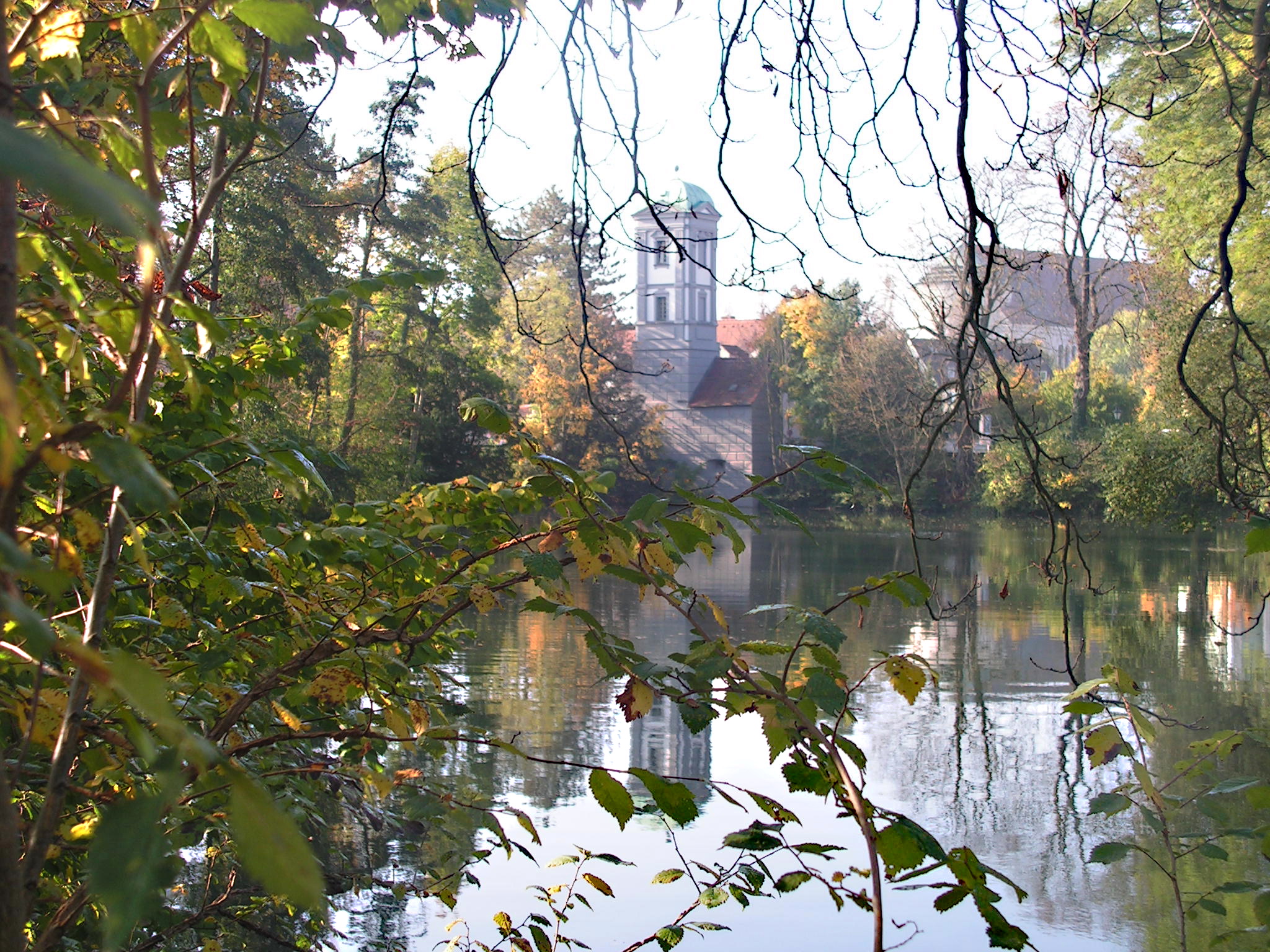 Im Vordergrund Äste eines Baumes, im Hintergrund ein Fluss und ein Turm.