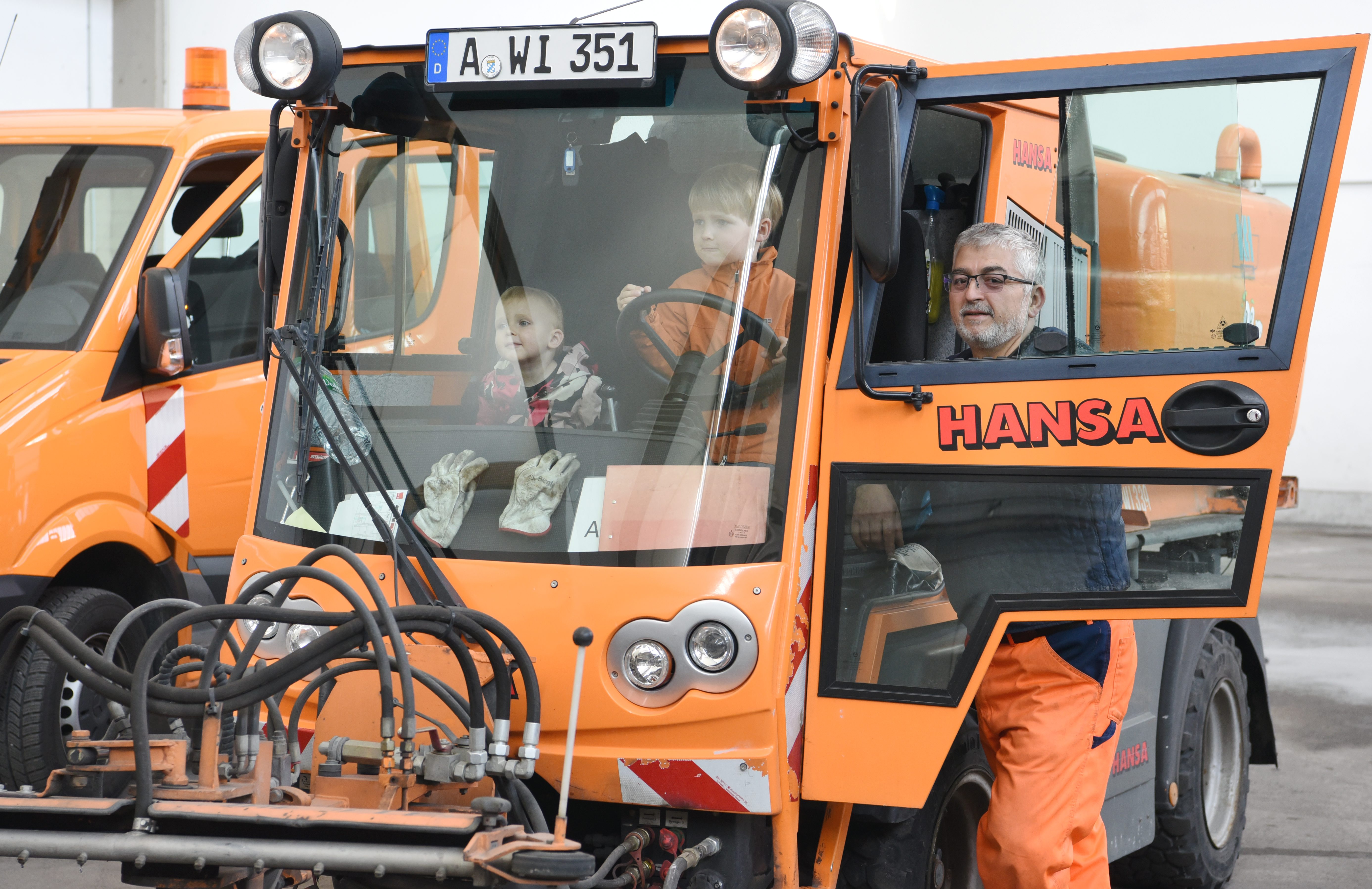 Zwei Kinder sitzen in einem Fahrzeug der Müllabfuhr. Ein Mitarbeiter erklärt ihnen etwas. 