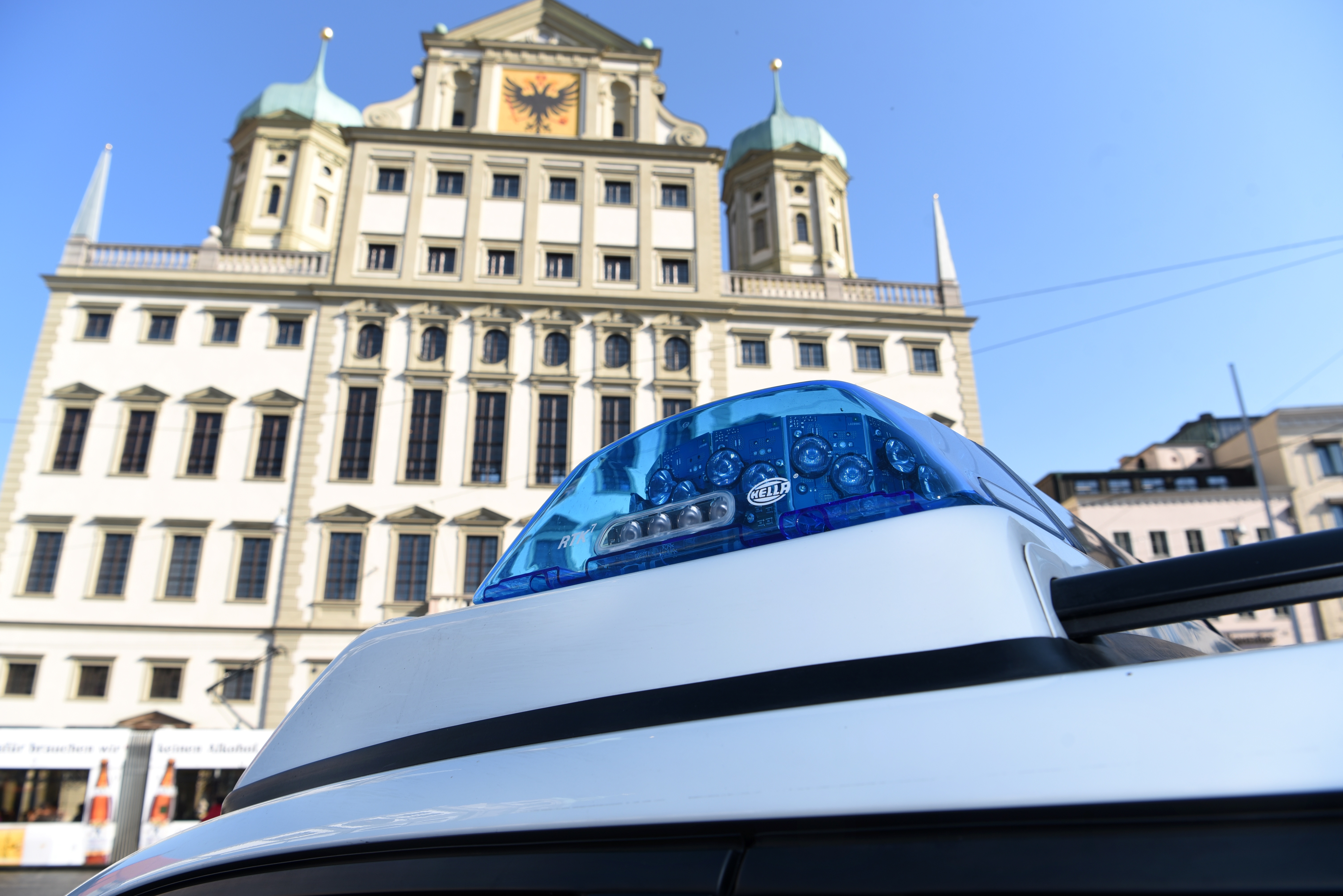 Vor dem Augsburger Rathaus ist im Vordergrund ein Blaulicht auf dem Dach eines Polizeiautos zu sehen