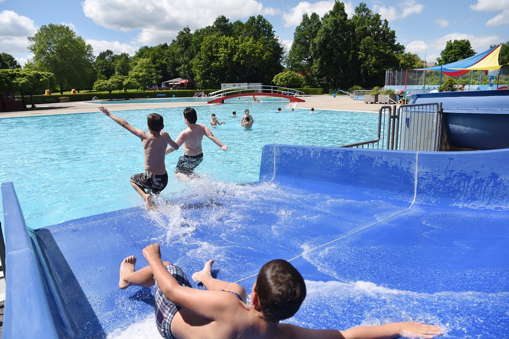 Drei Jugendliche rutschen über eine Wasserrutsche in ein Schwimmbecken eines Freibads