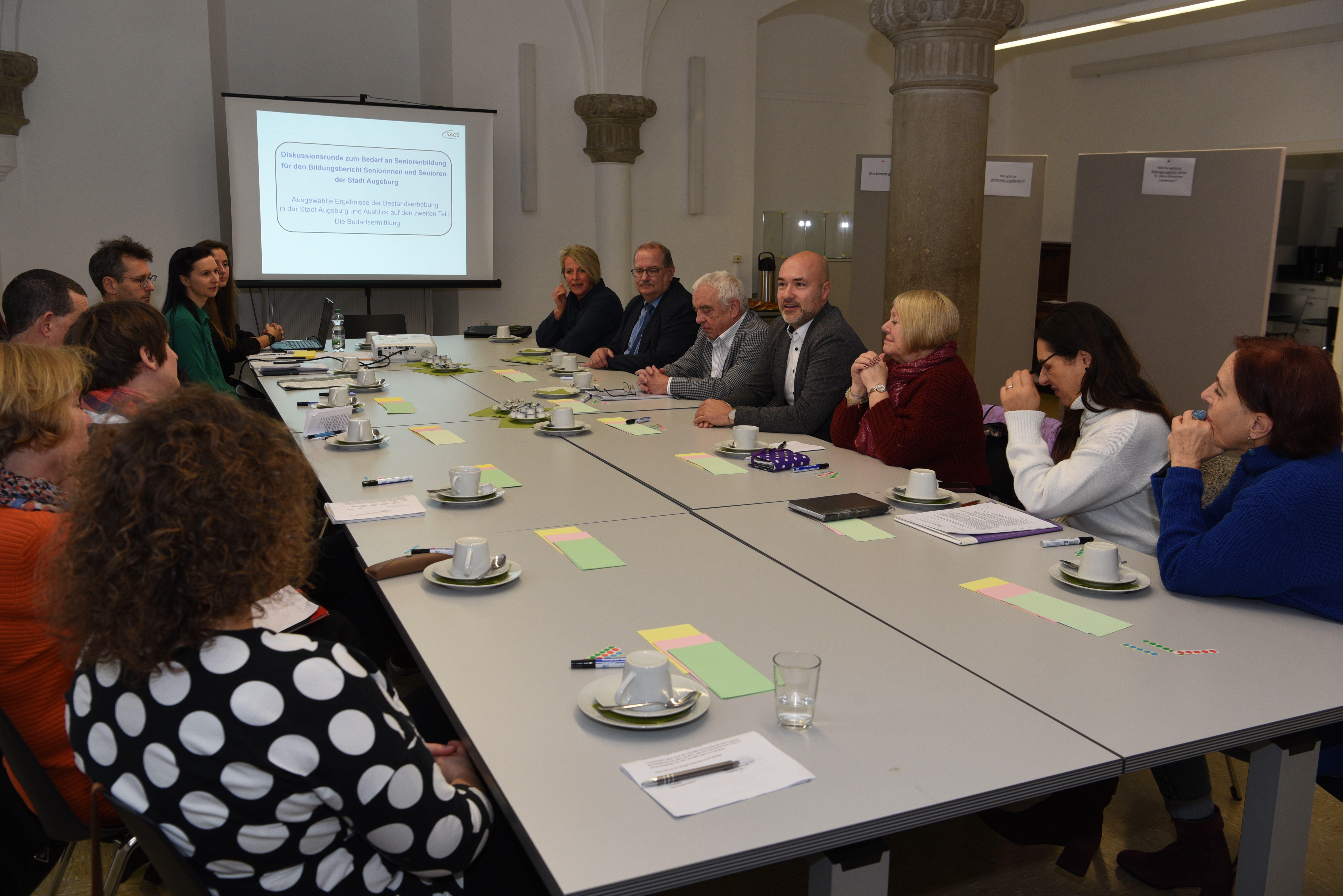 Etwa 15 Personen sitzen an einem großen Tisch.