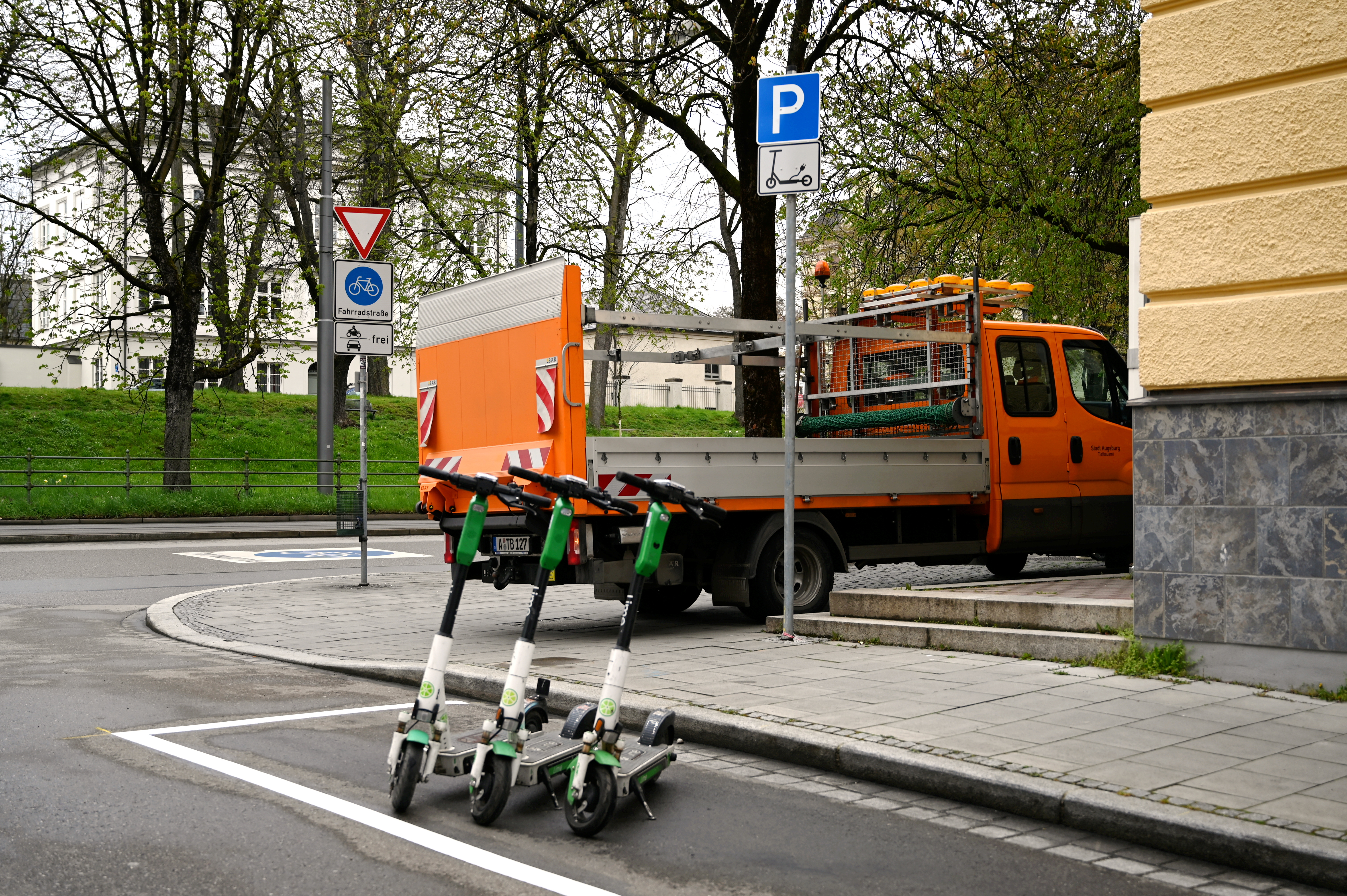 Drei Elektro-Roller stehen am Straßenrand in einer weiß umrandeten Fläche.