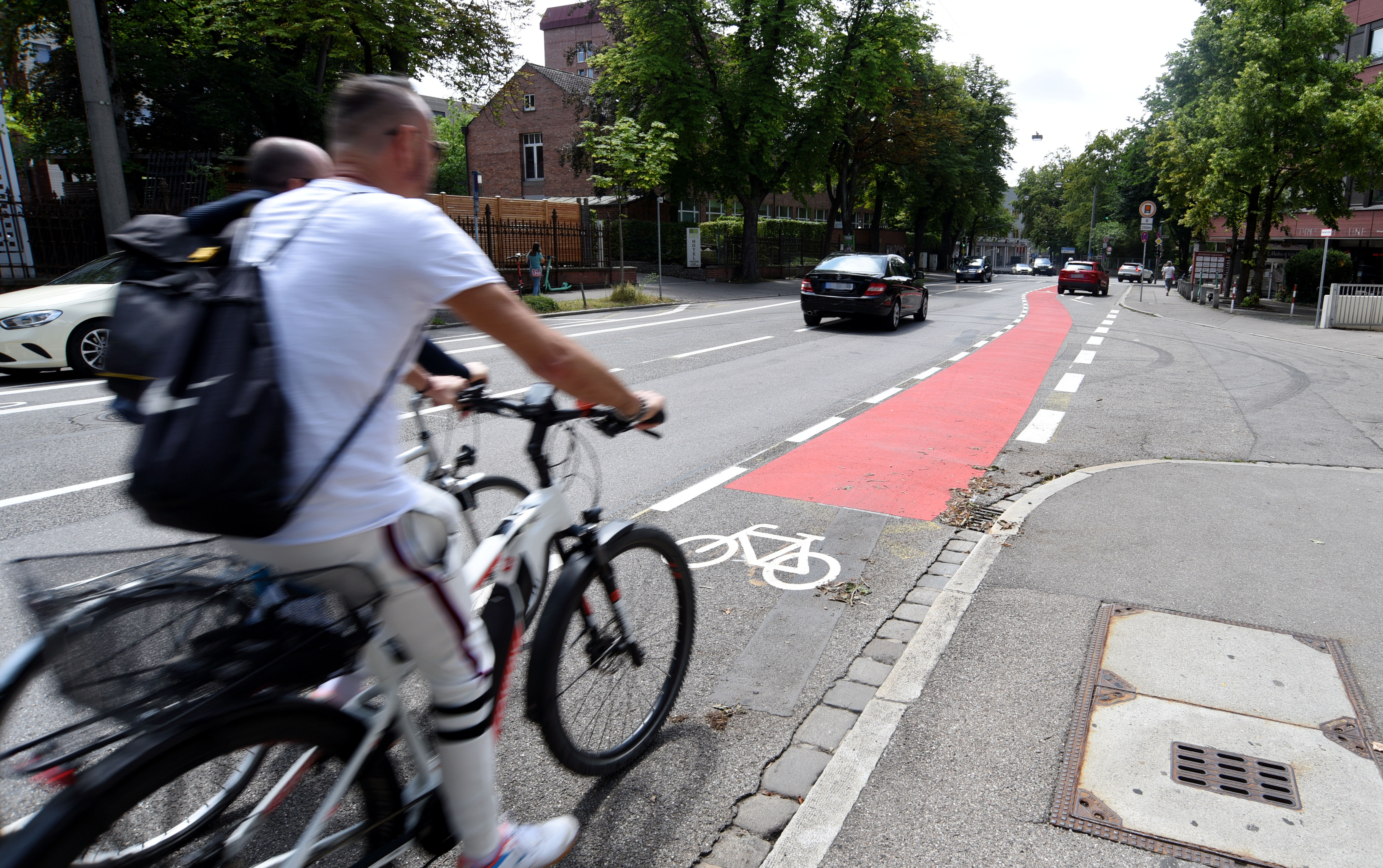 Zwei Radfahrer fahren auf dem neu markierten Radstreifen in der Fröhlichstraße. An einer Kreuzung ist der Radstreifen rot eingefärbt.