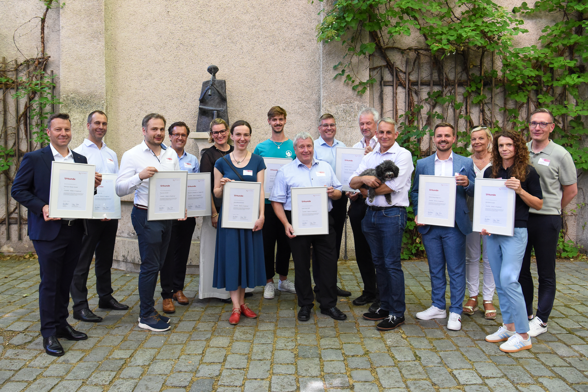 Gruppenbild mit Anerkennungsurkunden; ein Mann hält einen Pudel auf dem Arm