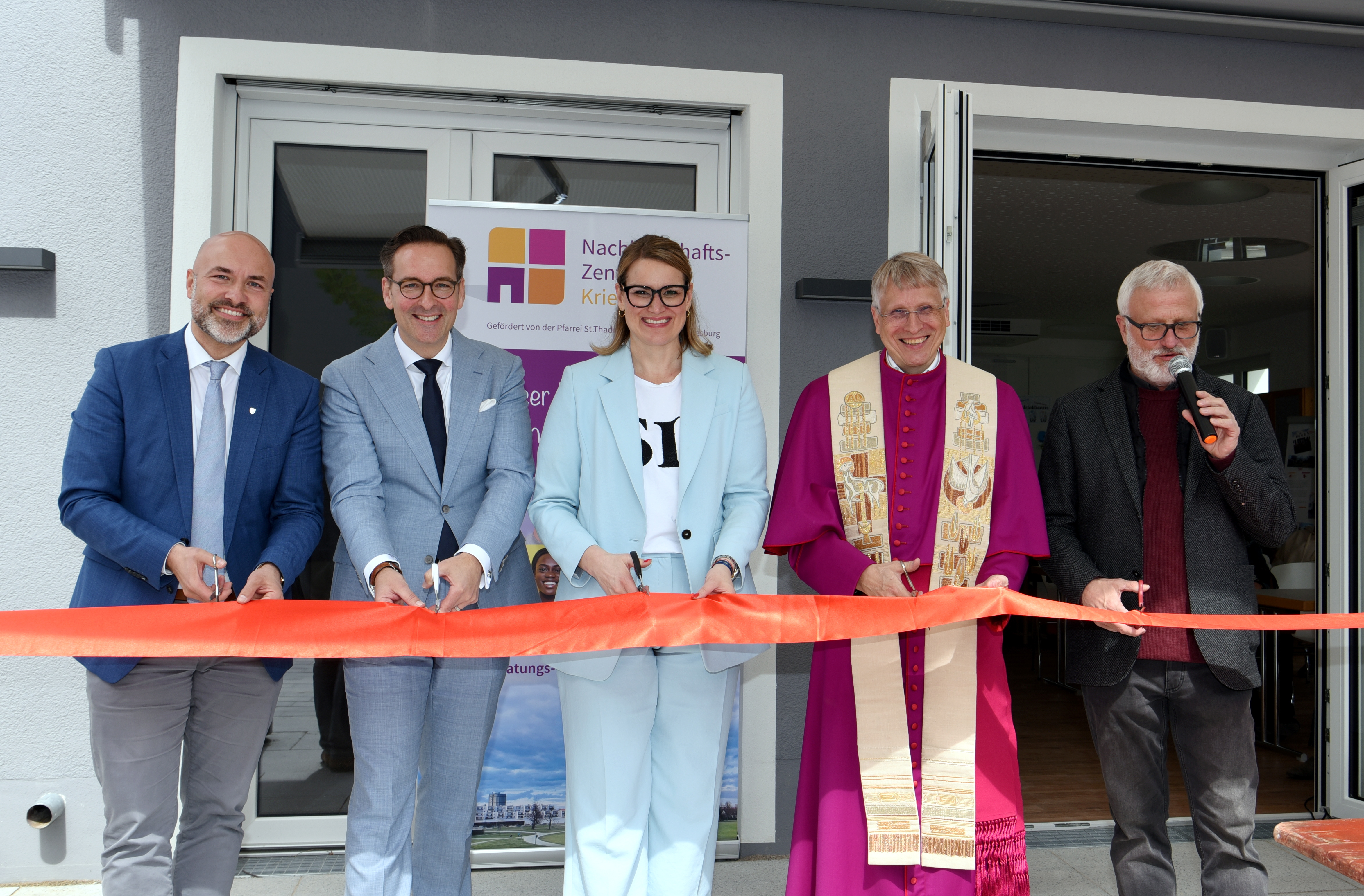 Fünf Menschen mit Scheren stehen an einem Roten Band und schneiden es durch. Hinter ihnen ist der Eingang zu einem Gebäude
