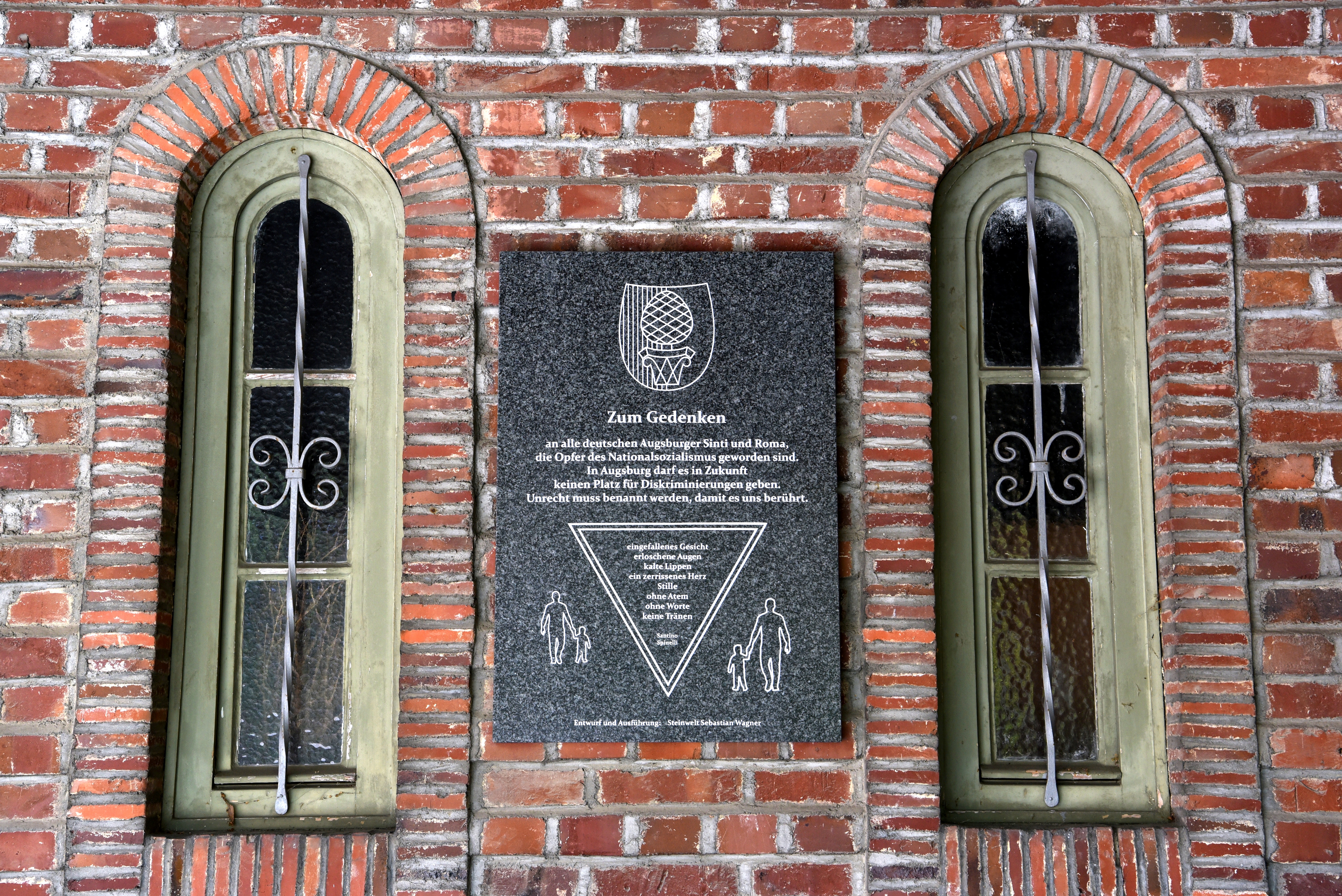 Gedenktafel zwischen zwei Fenstern an Backsteingebäude