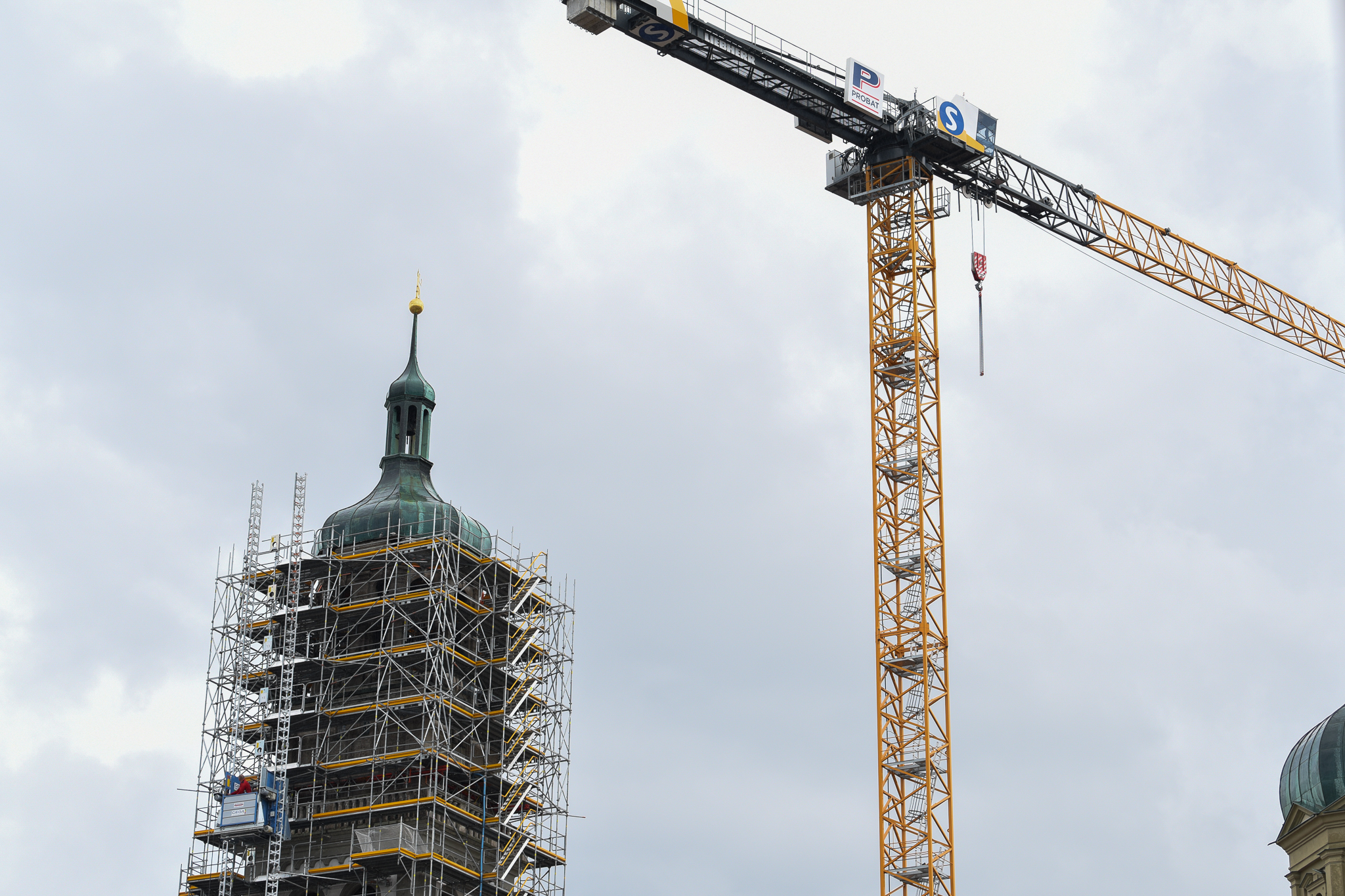 Die Spitze des Perlachturms. Der Turm ist mit einem Baugerüst verhüllt. Neben dem Turm steht ein großer Kran