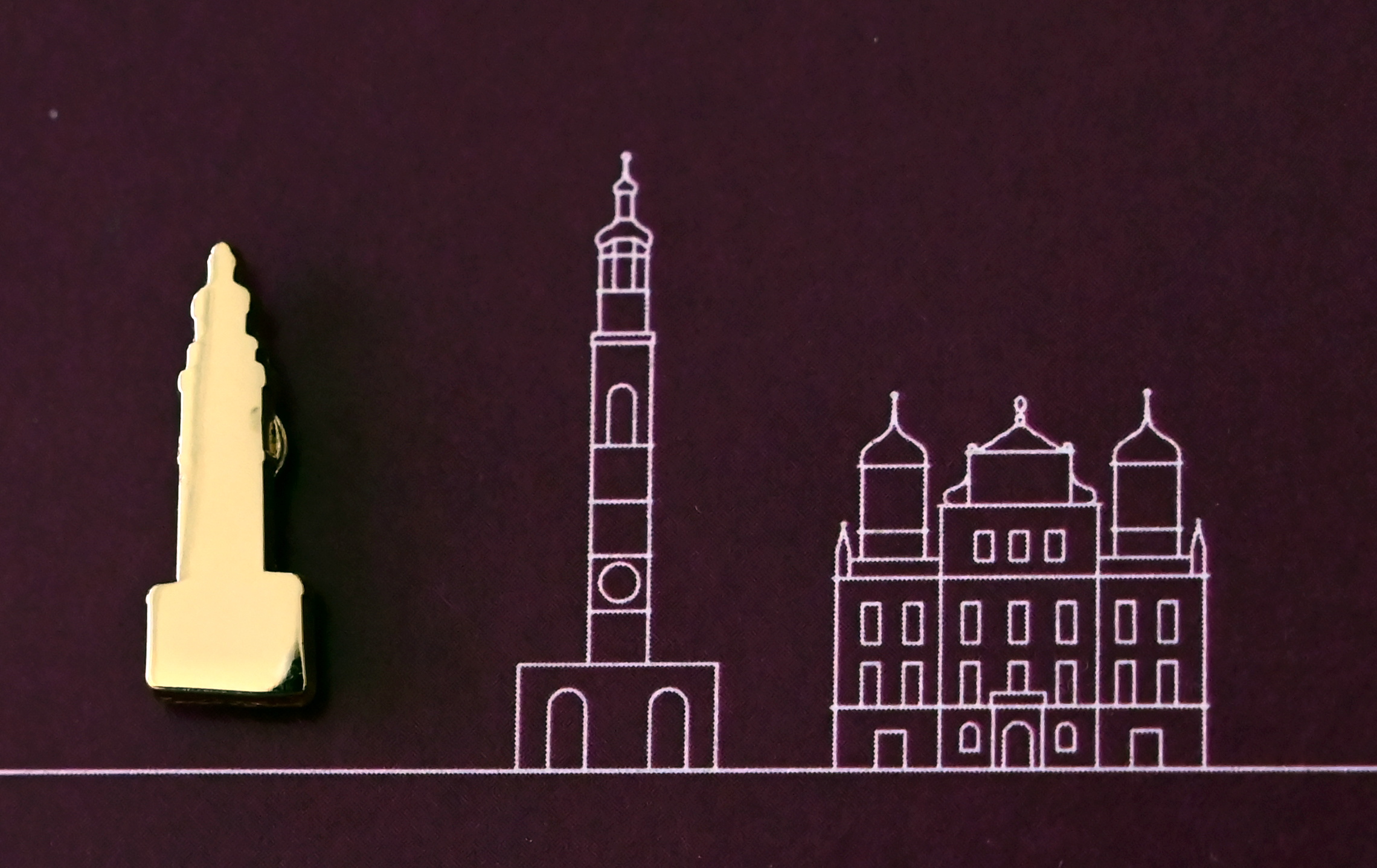 Eine goldene Miniatur des Perlachturms liegt neben einer Zeichnung von Perlachturm und Rathaus