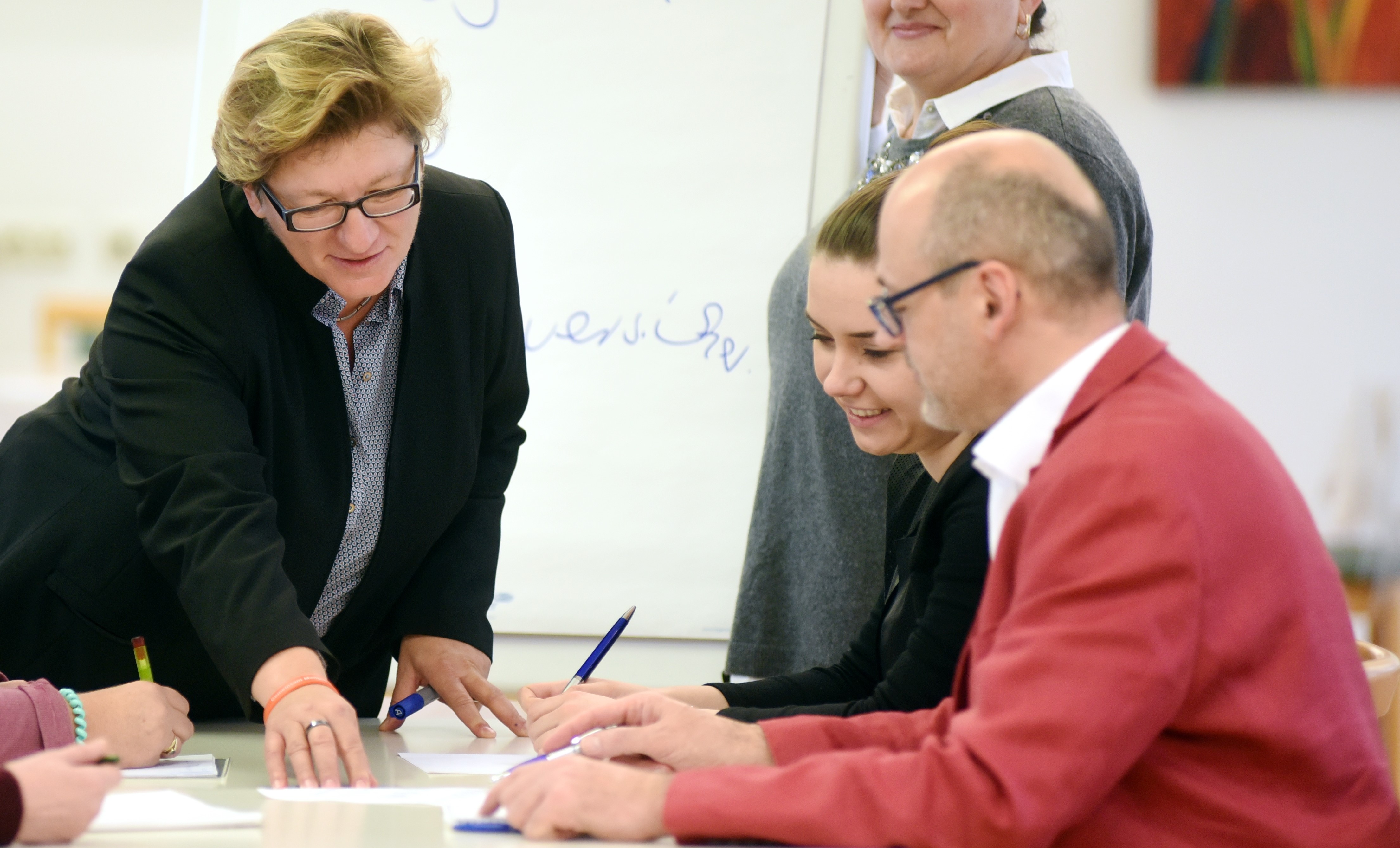 Eine Frau zeigt zwei Menschen auf einem Papier etwas. 
