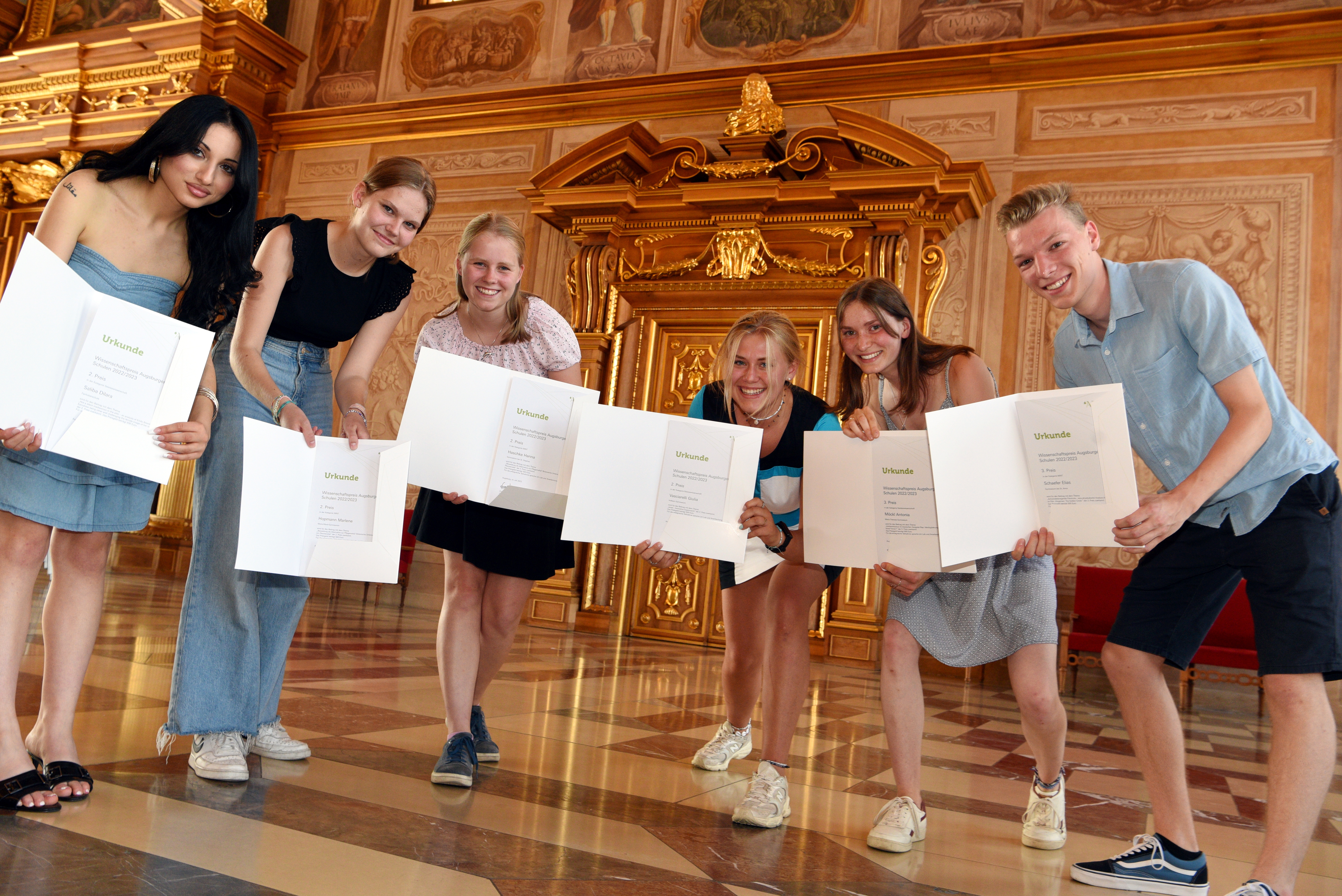 Sechs Schülerinnen und Schüler stehen im Goldenen Saal. Sie halten Urkunden in die Kamera.