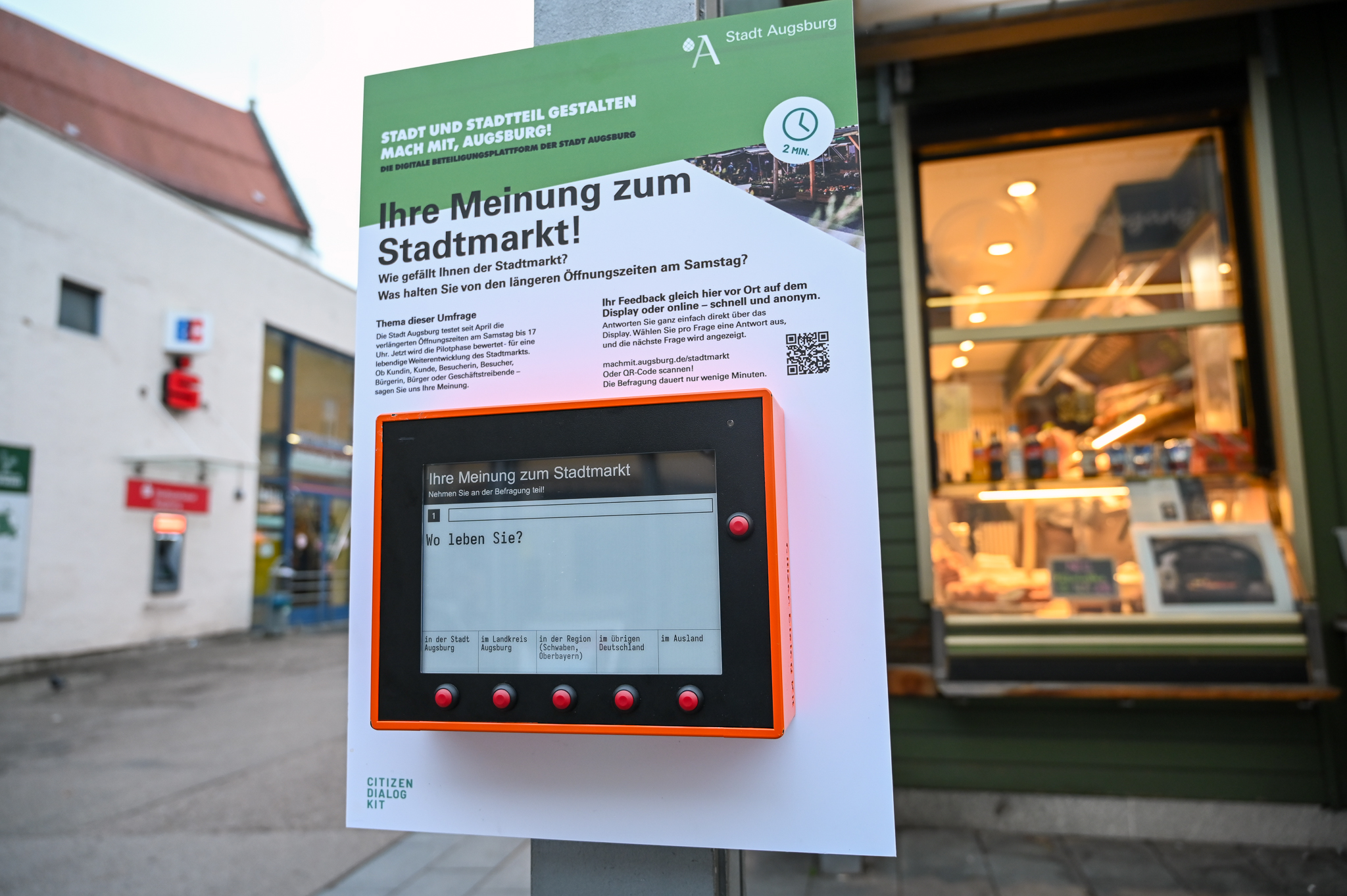 rechteckiges Display auf einer Erklärtafel, im Hintergrund ein Bäckereistand auf dem Stadtmarkt