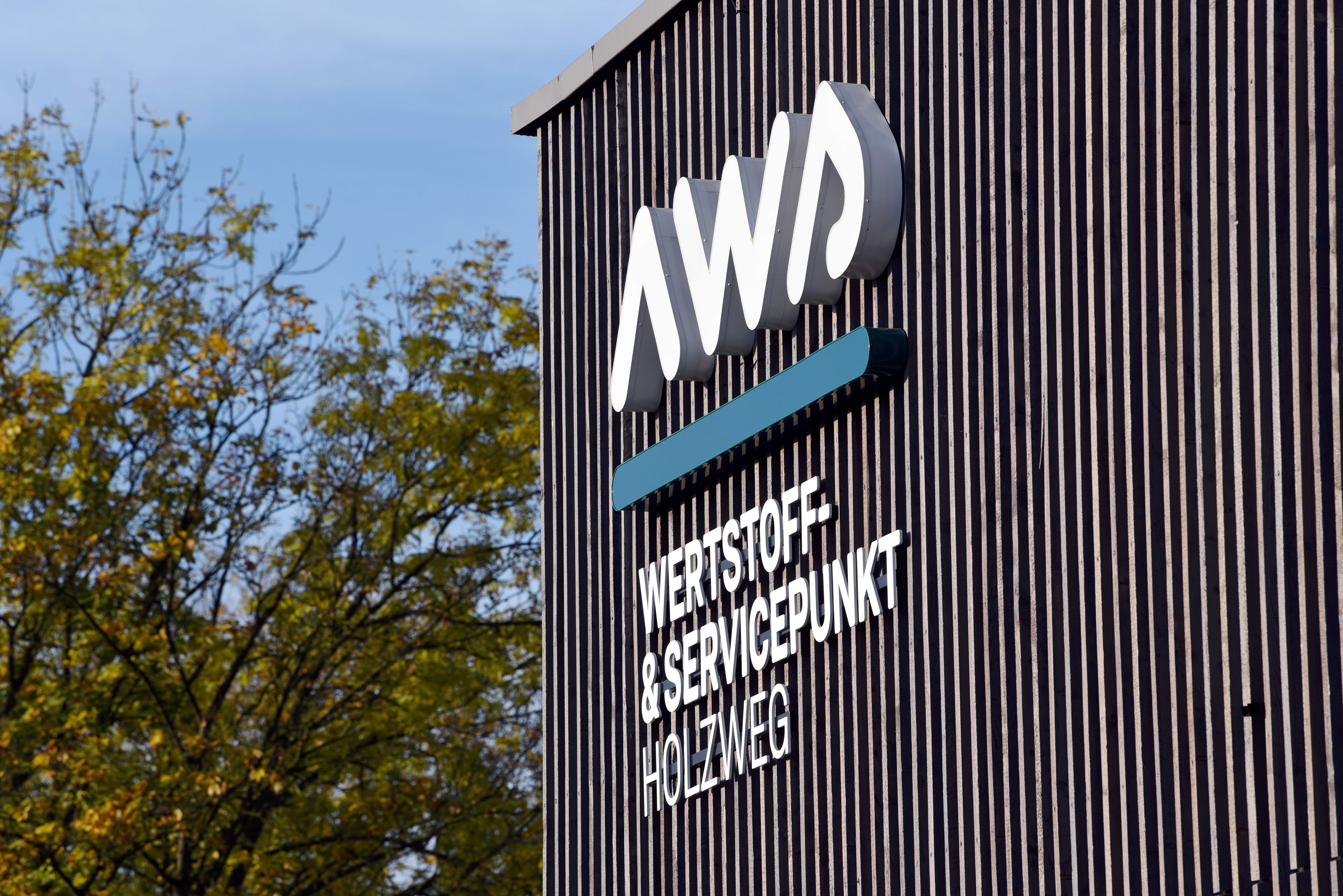 Ein hölzernes Gebäude mit der Aufschrift "aws. Wertstoff- & Servicepunkt Holzweg"