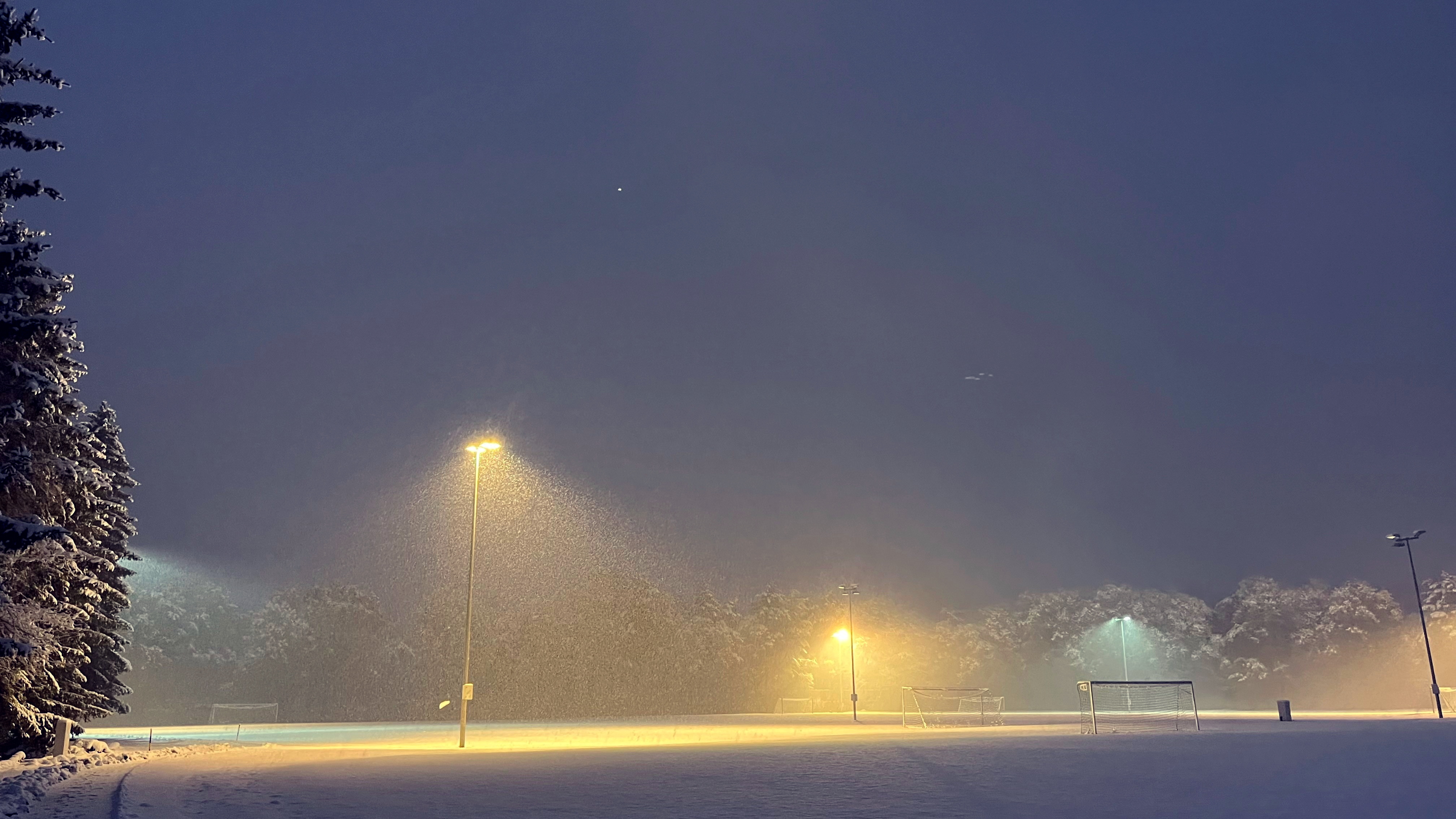 Sportplatz bei Schneefall am Abend.