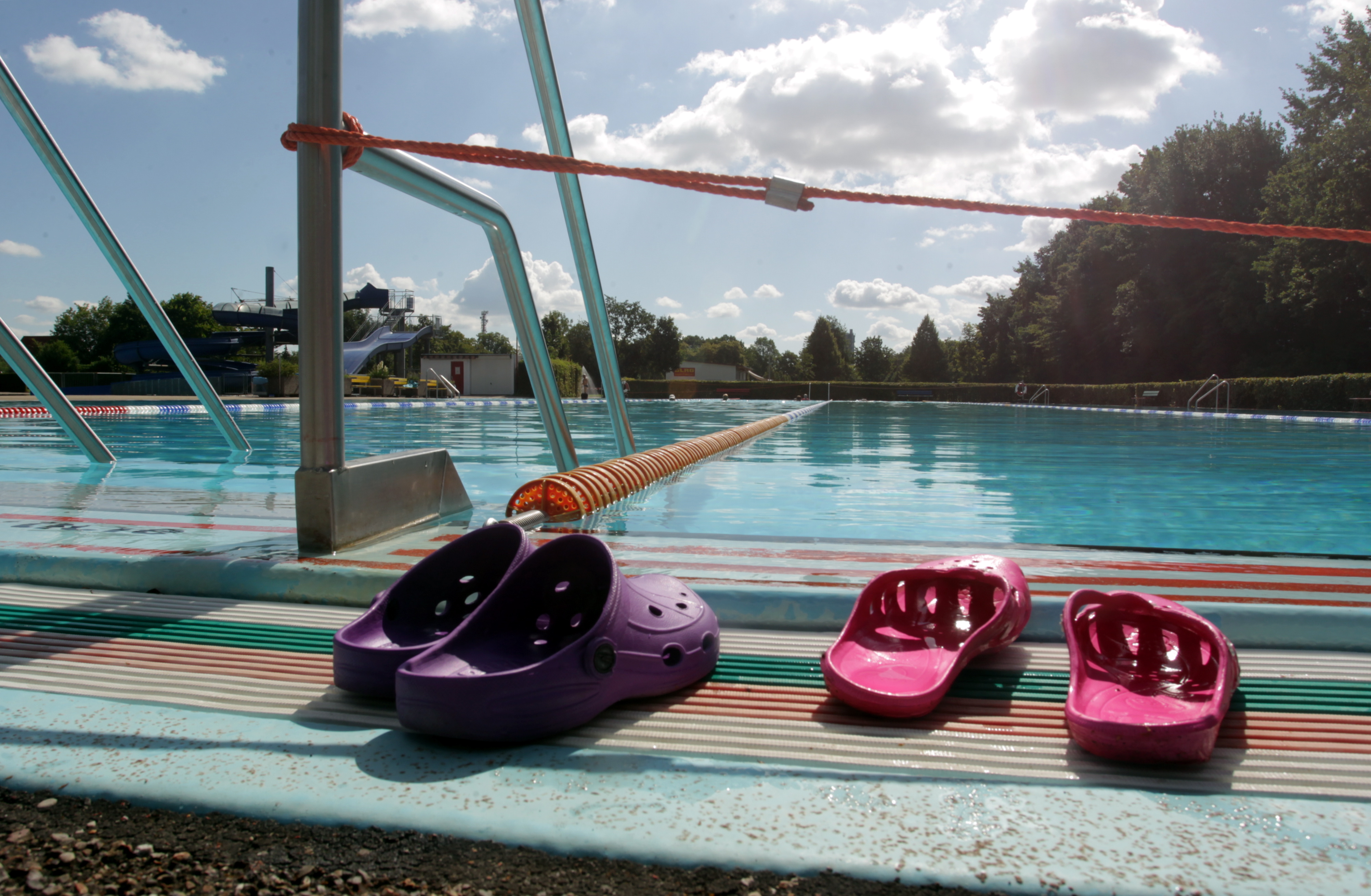 ein pinkes und ein lilanes Badeschuh-Paar stehen vor einem leeren Schwimmbecken im Freien. 