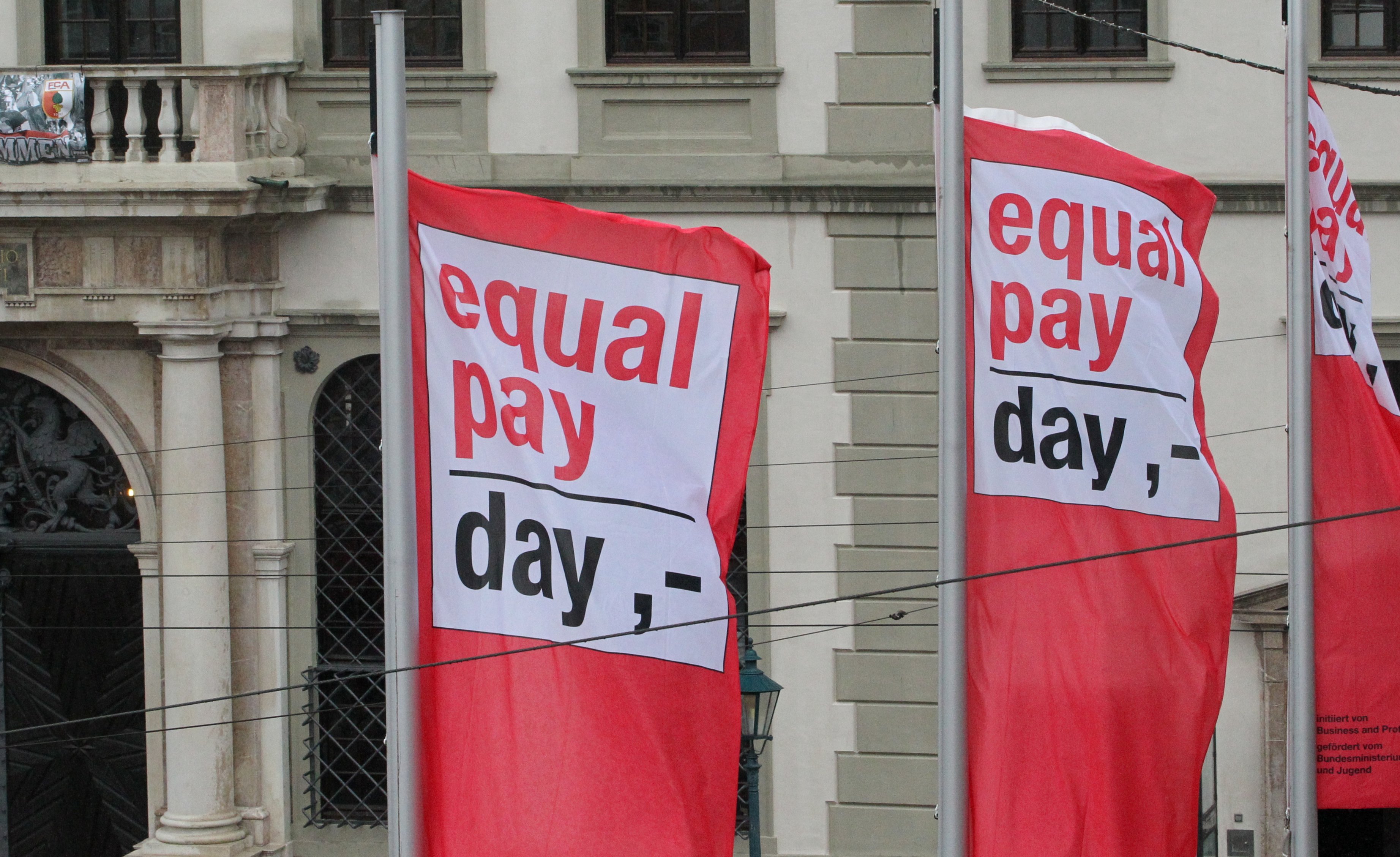drei Fahnen auf dem Rathausplatz mit dem Aufschrift "Equal Pay Day"