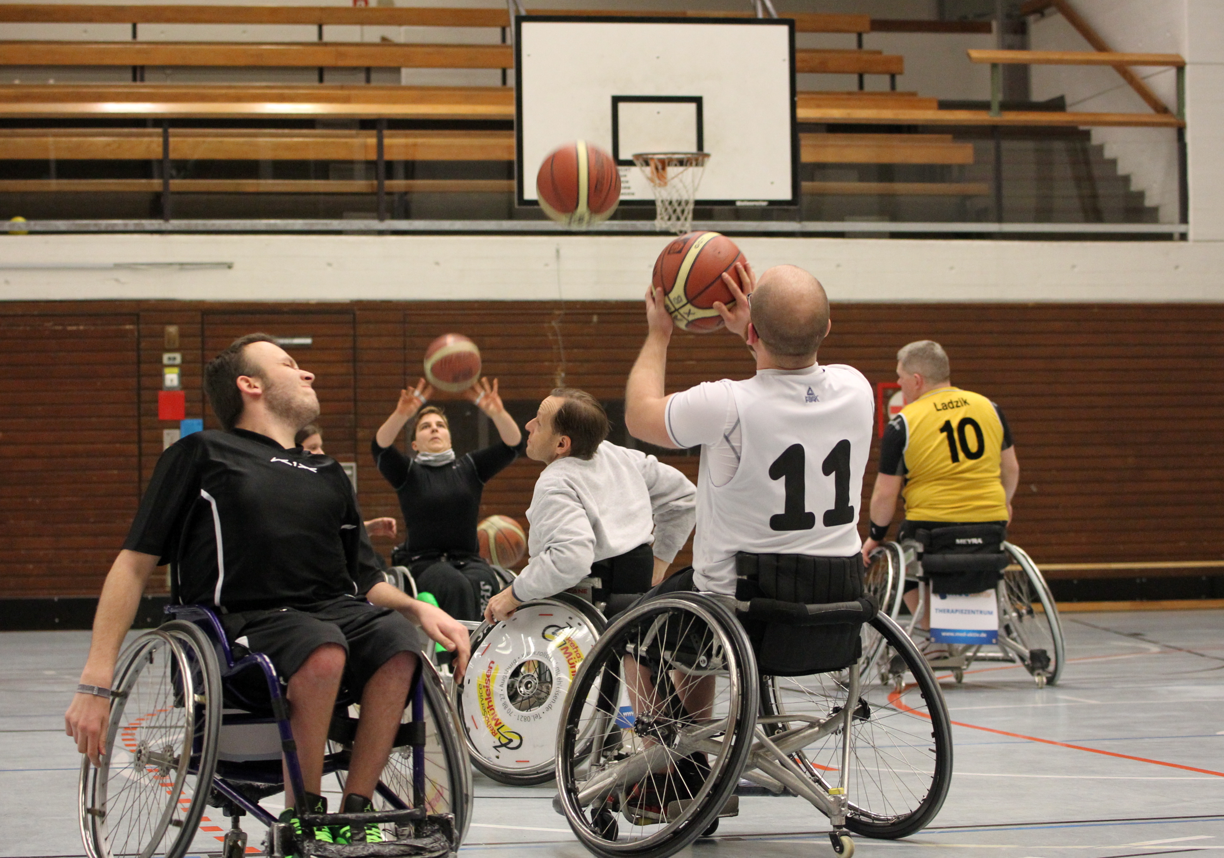 Männer im Rollstuhl spielen Basketball, einer wirft gerade einen Korb