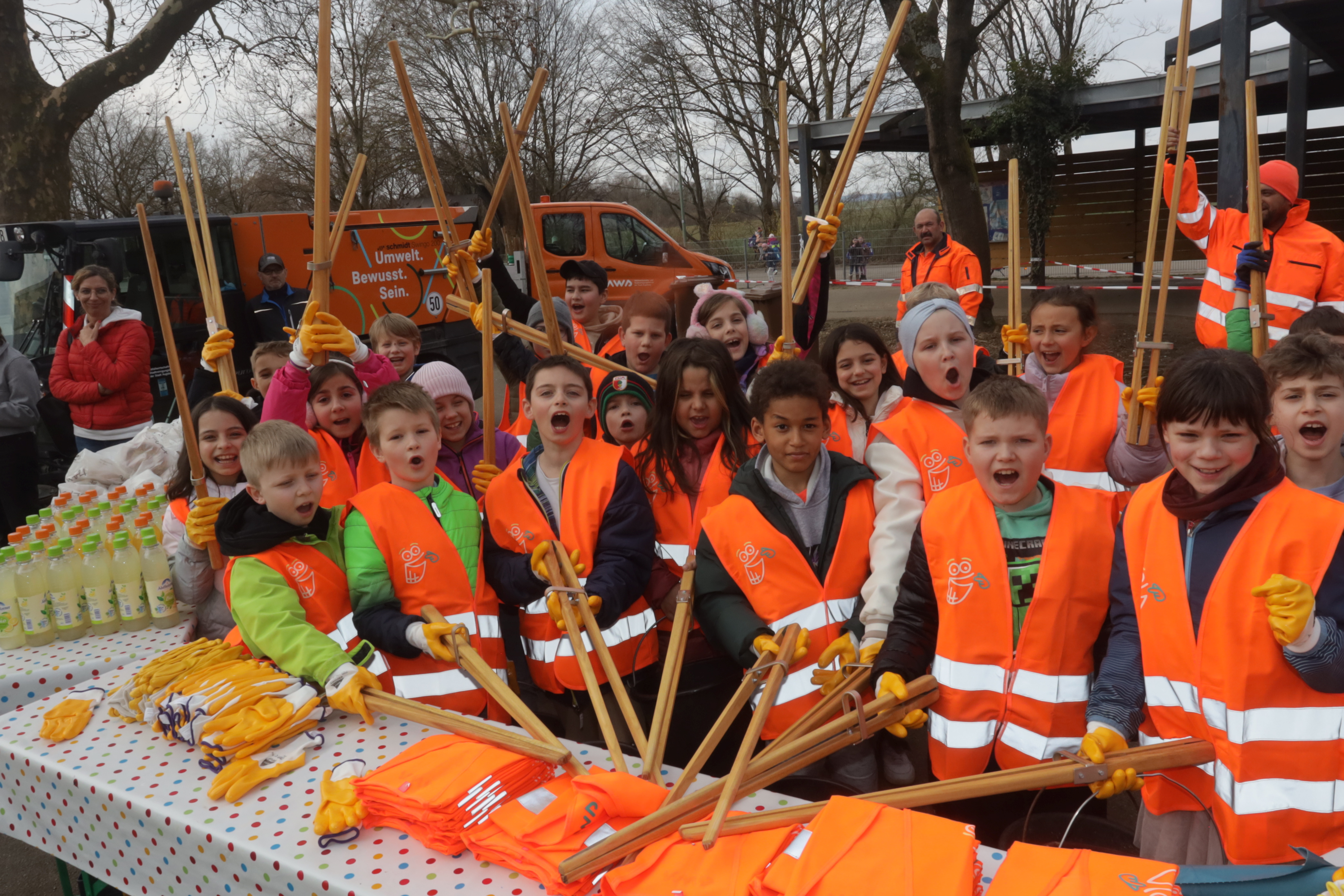 Viele Kinder in orangenen Westen mit Holz-Zangen rufen fröhlich in die Kamera